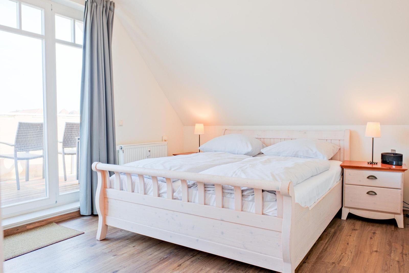 Schlafzimmer mit Doppelbett, Nachttisch und Fenster zum Balkon.