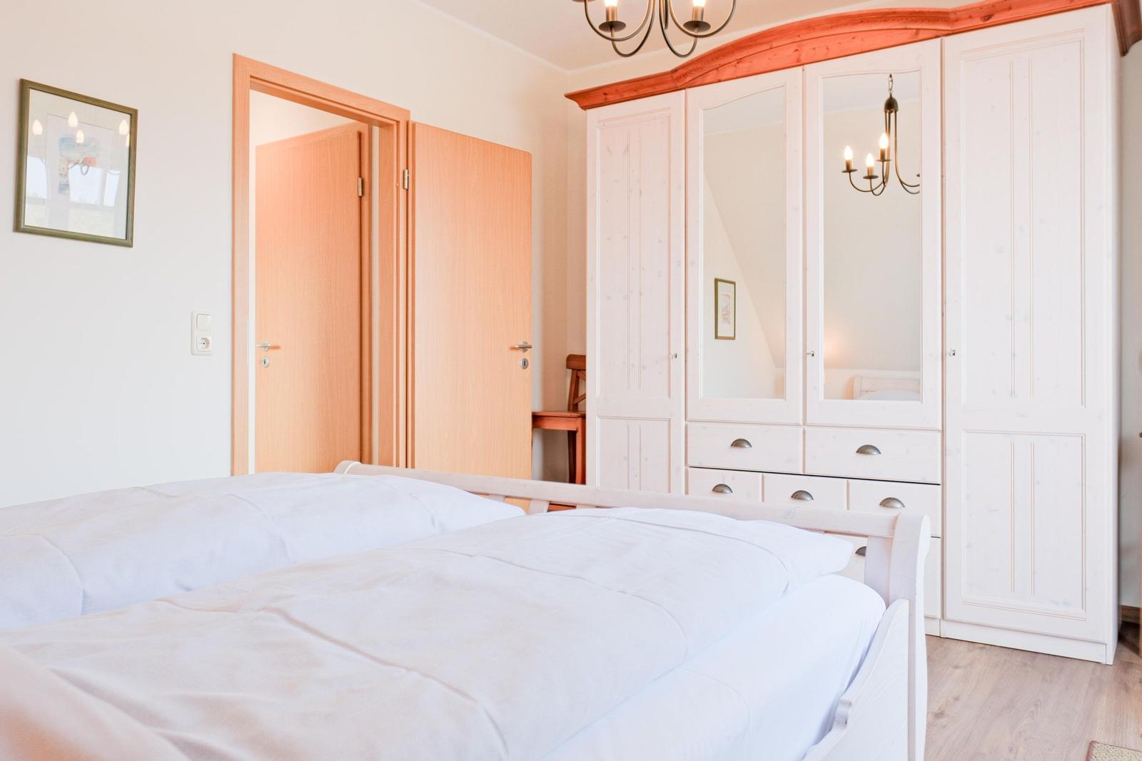 Schlafzimmer mit weißem Bett, Kleiderschrank und Tür.