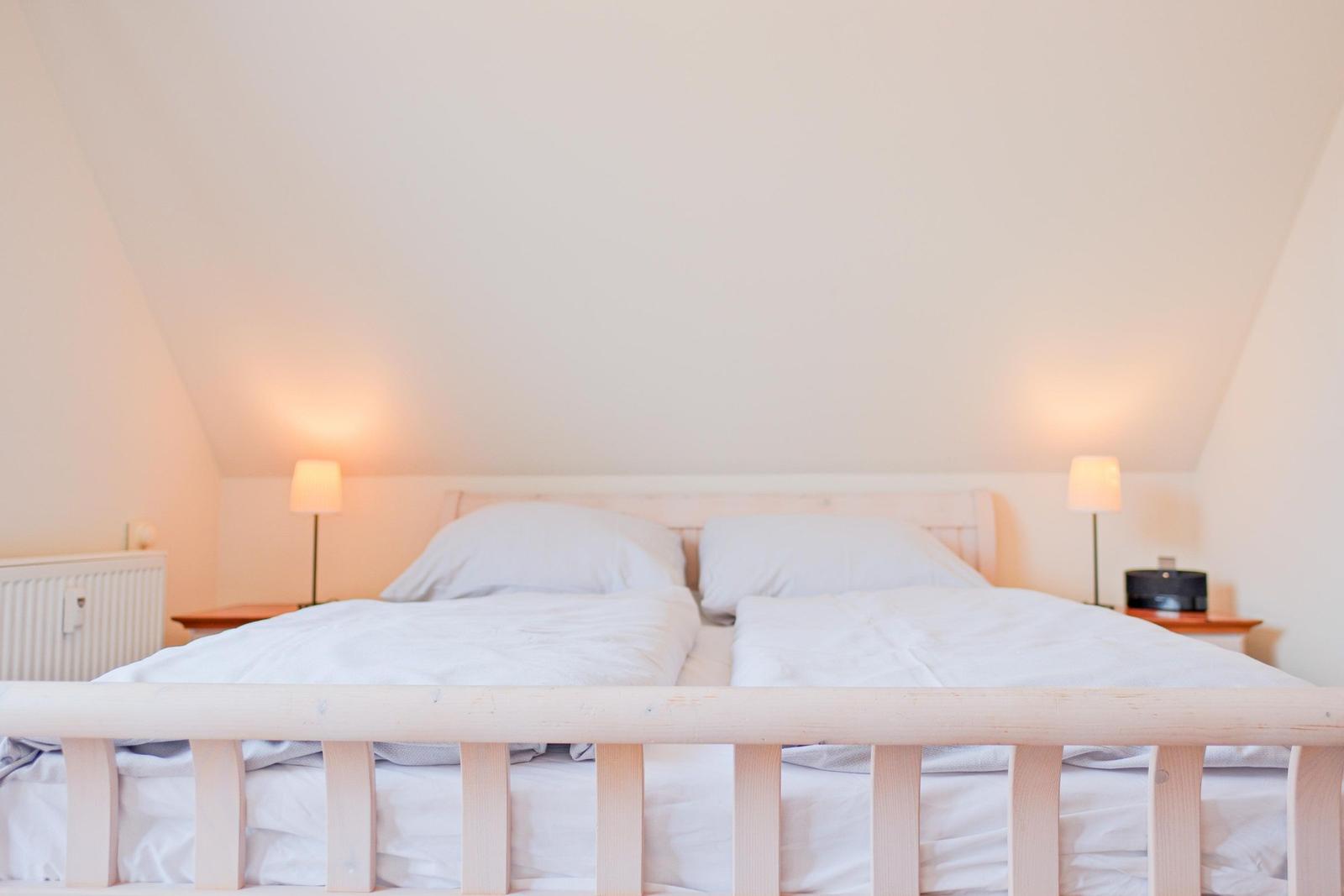 Schlafzimmer mit Doppelbett, zwei Nachttischen und Lampen unter schrägen Wänden.