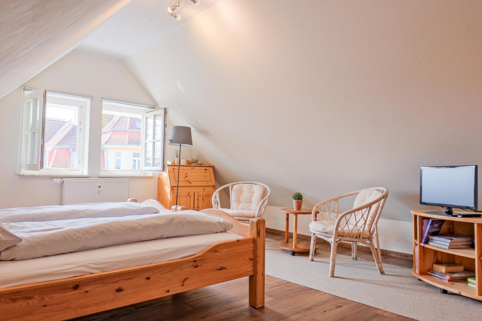 Schlafzimmer mit Dachschräge, Bett, zwei Stühlen und Fernseher.