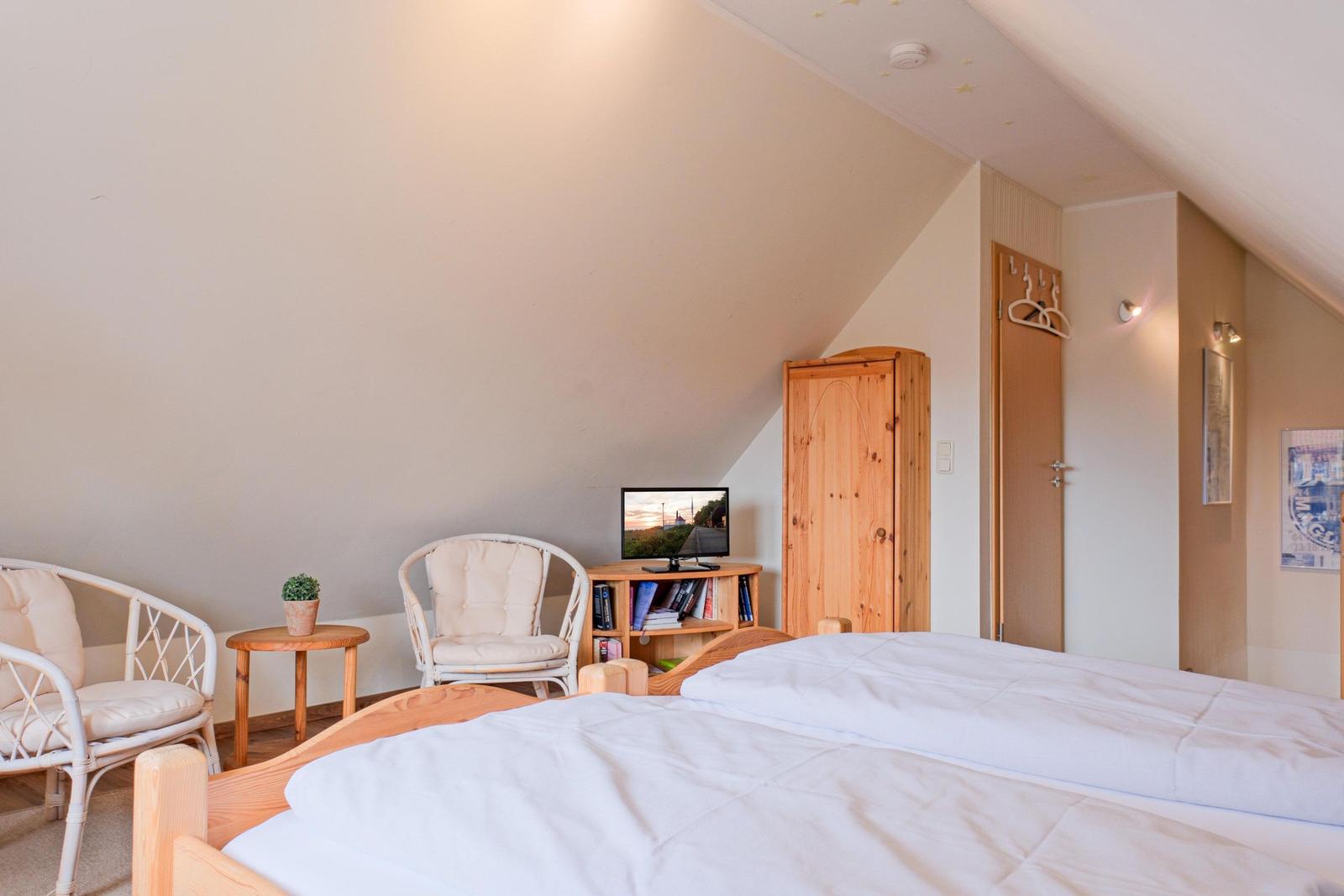 Schlafzimmer mit Doppelbett, zwei Stühlen, kleinem Tisch und Fernseher.