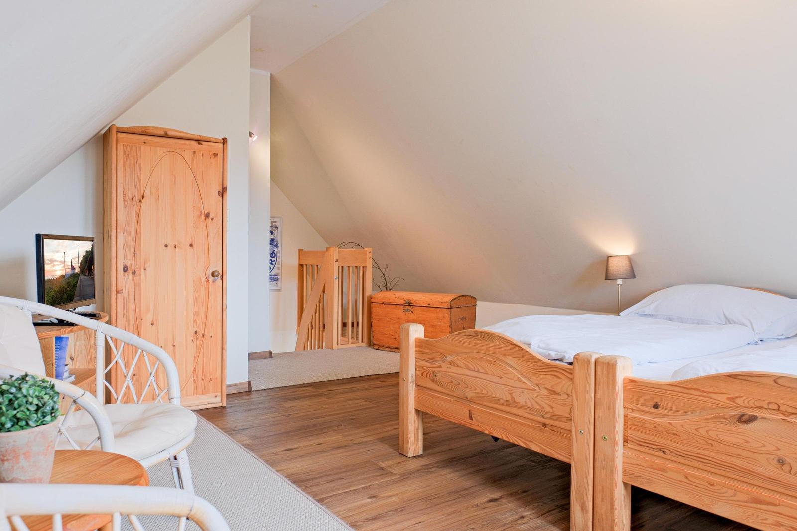 Schlafzimmer mit Holzbett, Kleiderschrank und Fernseher unter Dachschräge.