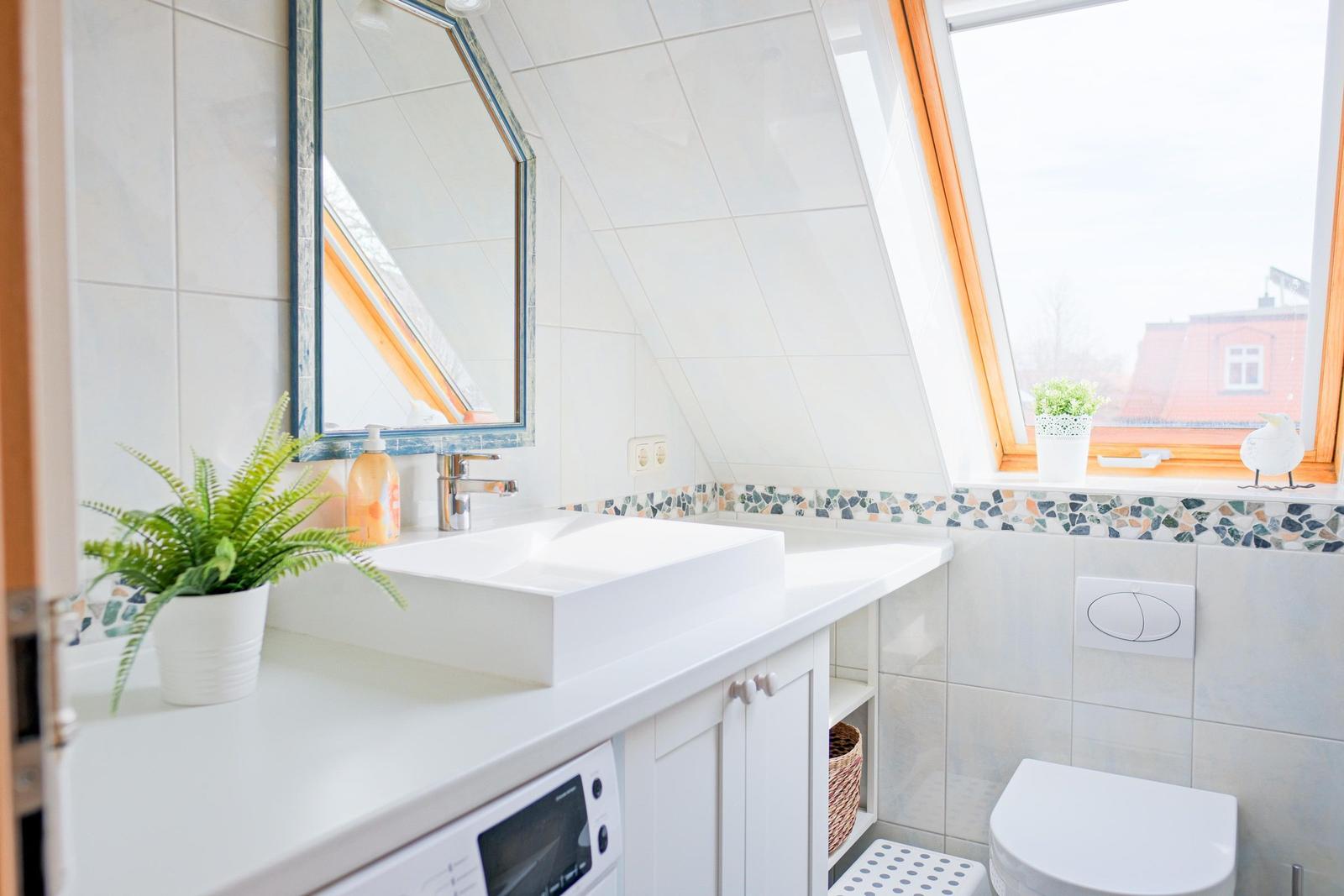Badezimmer mit Waschbecken, Spiegel und Fenster. Weiße Fliesen und Mosaikverkleidung.