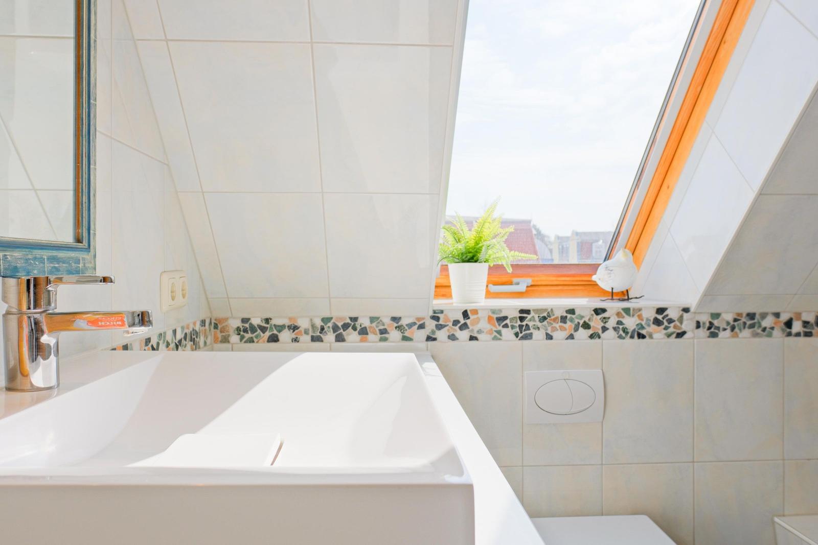 Badezimmer mit Waschbecken, Spiegel und Dachfenster mit Pflanze.