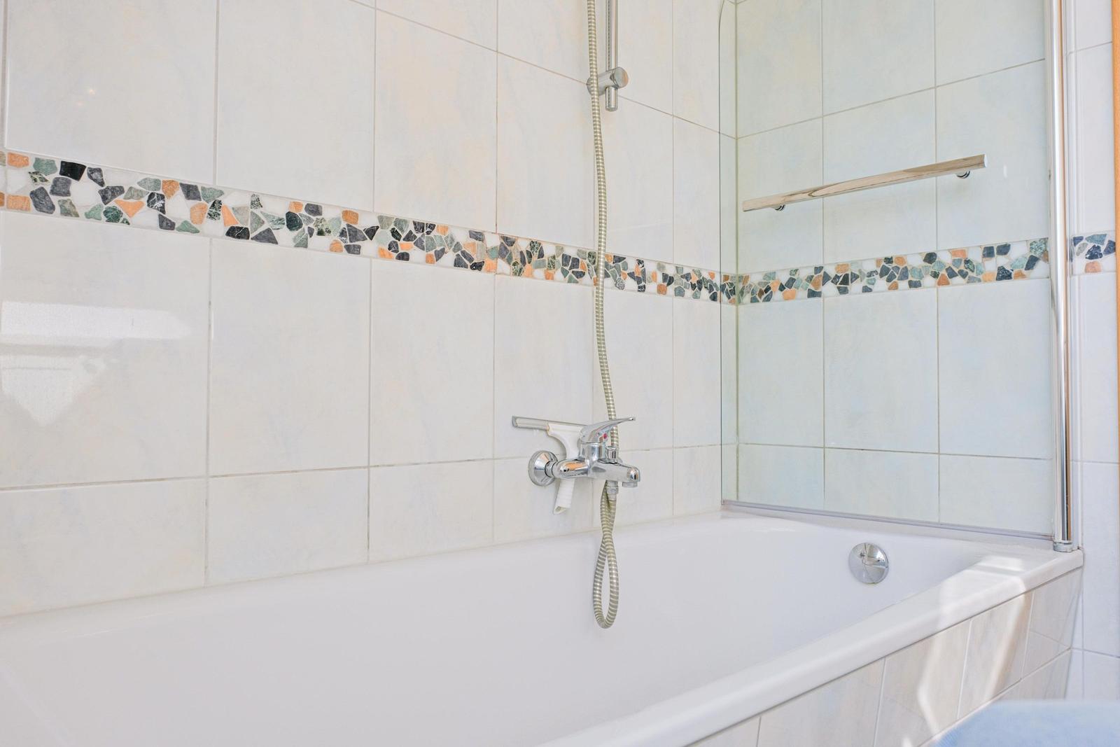 Bad mit Badewanne, Duschkopf und Mosaikfliesen an der Wand.