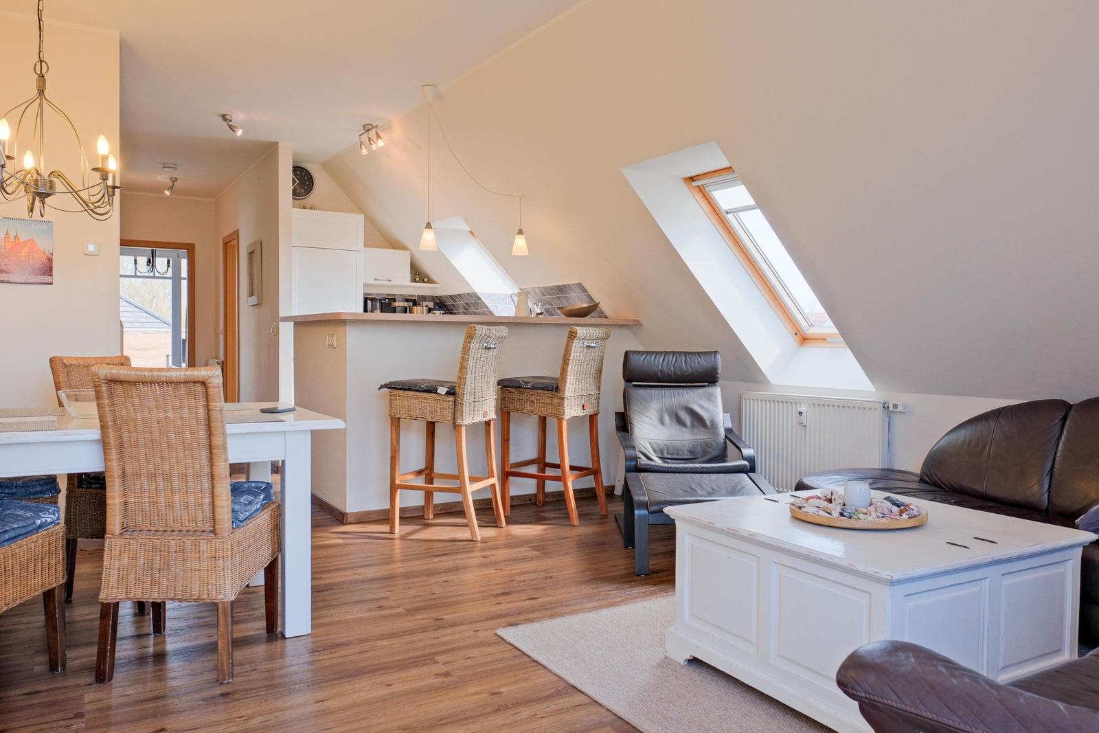 Wohn- und Essbereich mit Dachschrägen, Sitzgelegenheiten und Fenster. Holzboden und weiße Möbel.