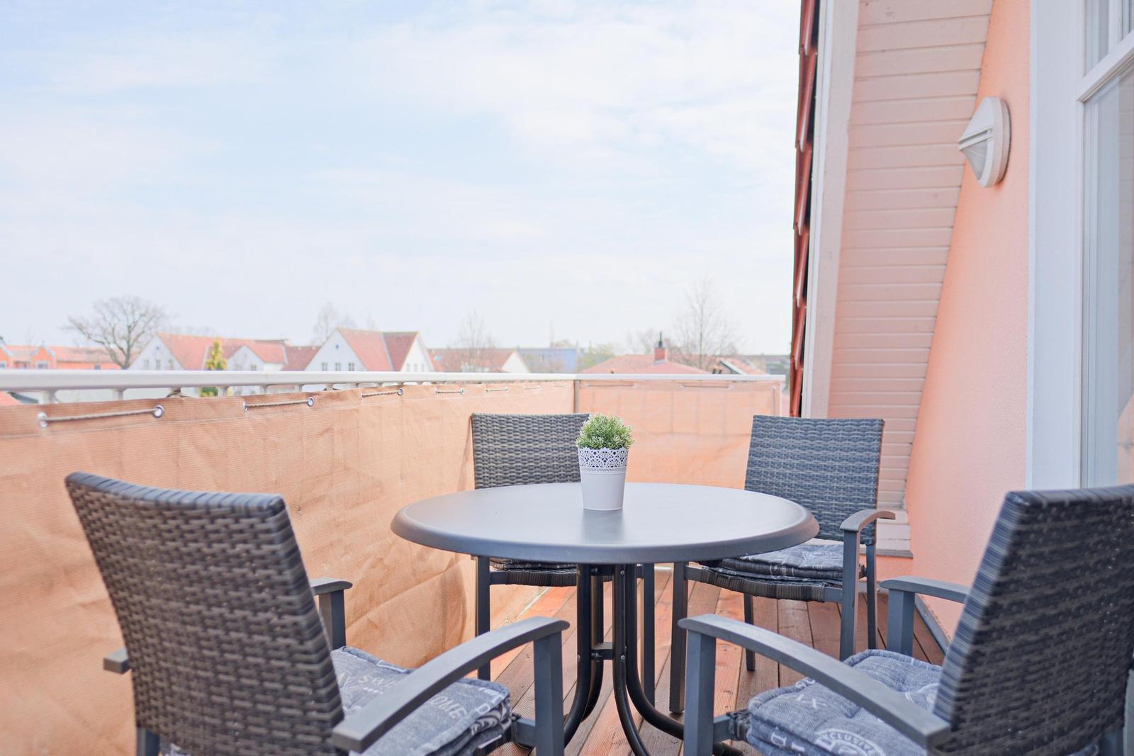 Terrasse mit Tisch und vier Stühlen, Blick auf Wohngebiet.