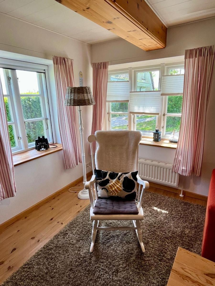 Raum mit Schaukelstuhl, Fenstern und Holzbalken an der Decke.