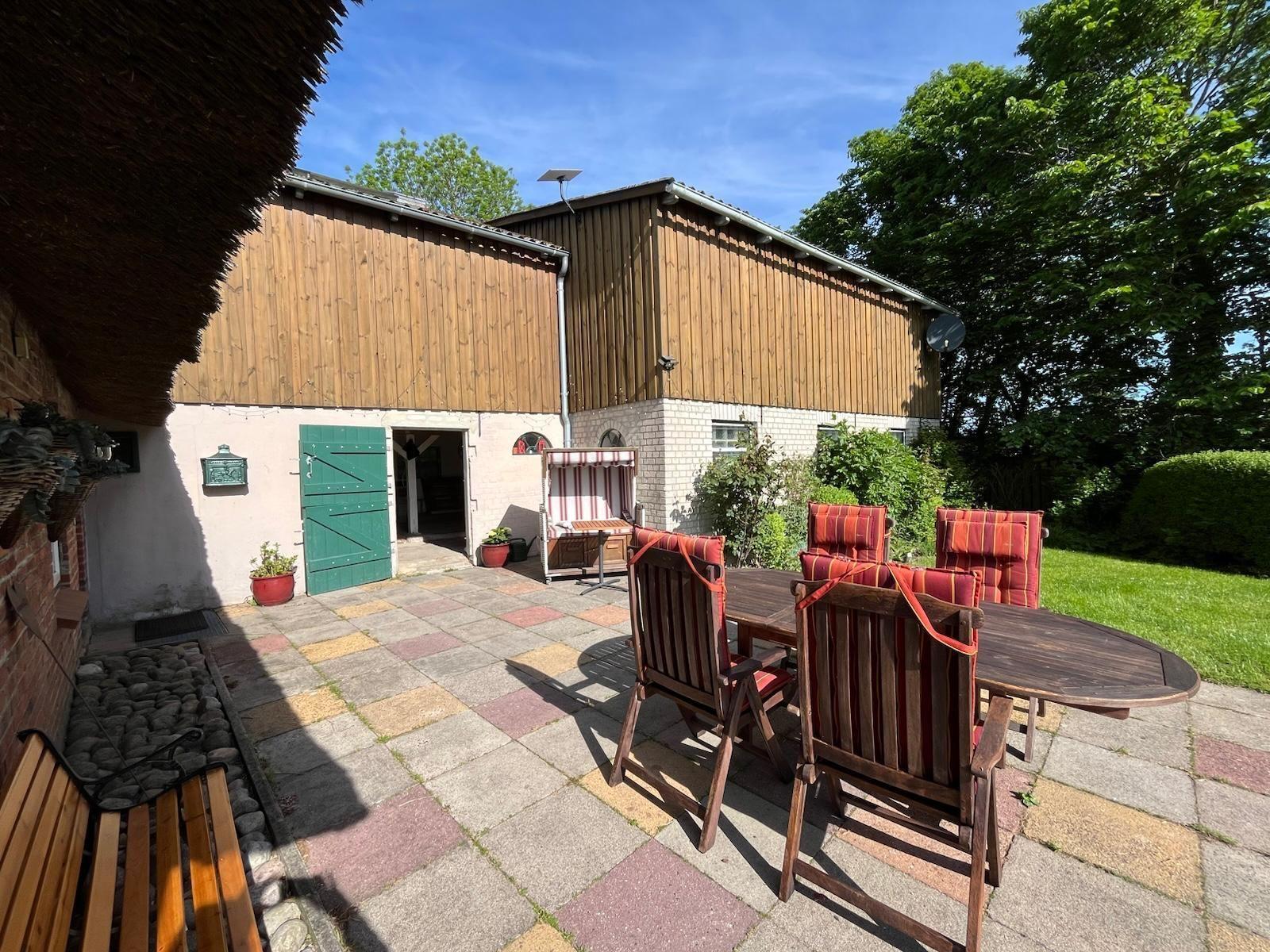 Terrasse mit Tisch und Stühlen vor Holzhaus mit grüner Tür.
