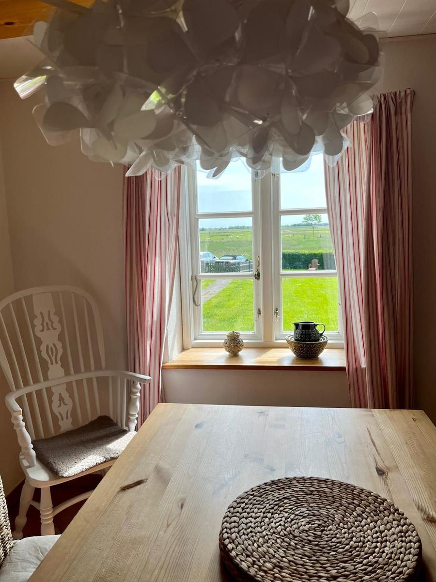 Esszimmer mit Holztisch, Stuhl und Blick auf grünes Feld durch Fenster.