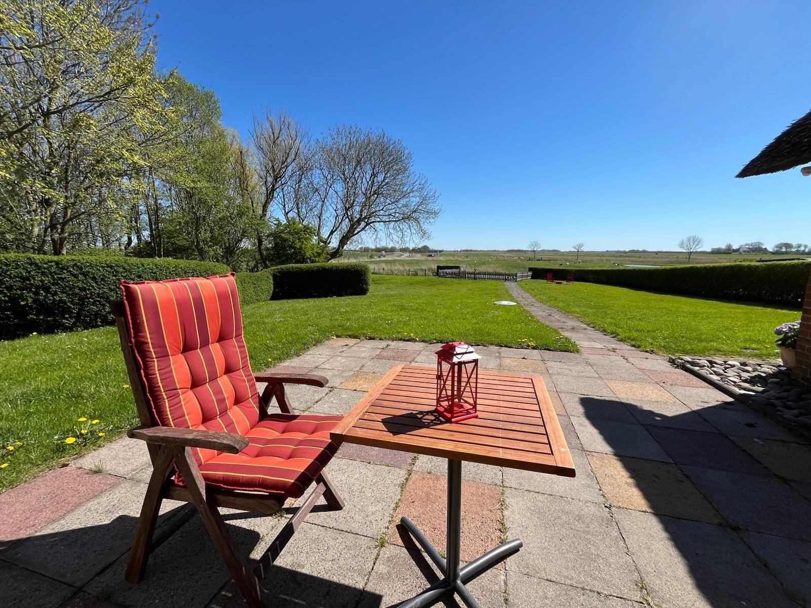 Roter Sitzplatz mit Tisch auf Terrasse. Blick auf grünen Garten und Wald.
