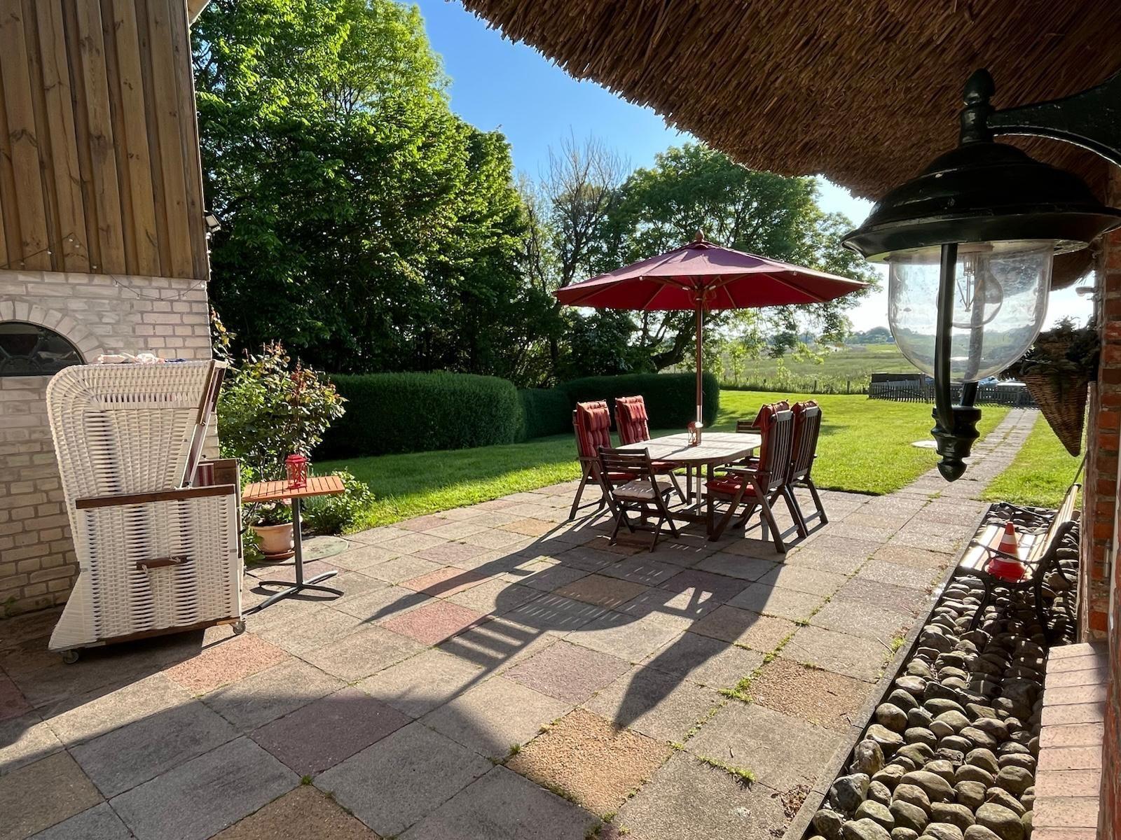 Terrasse mit Tisch, Stühlen und Sonnenschirm. Hinterhof mit Rasen und Bäumen.