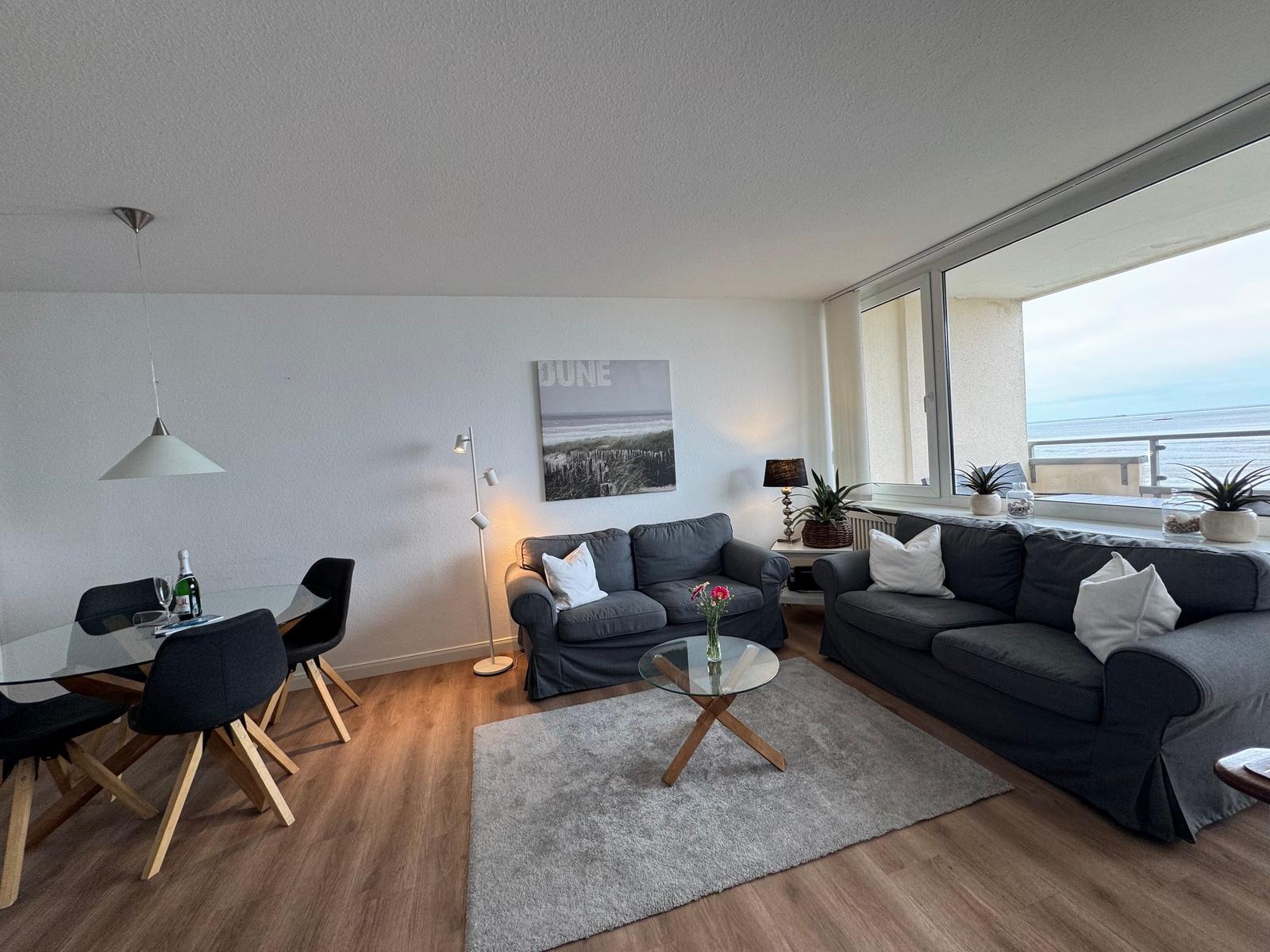 Wohn- und Essbereich mit Blick aufs Meer. Zwei Sofas, Tisch, Stühle und Wandbild.