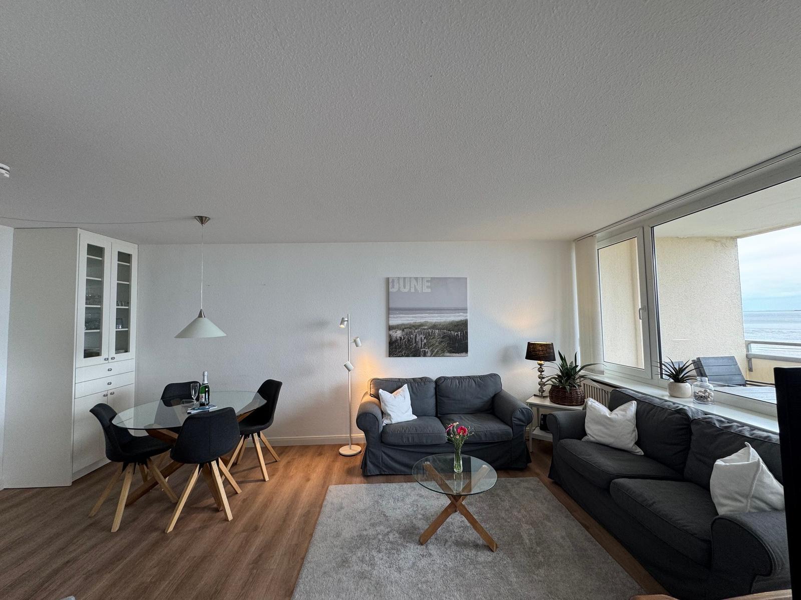 Wohn- und Essbereich mit Sofa, Tisch und Fensterblick aufs Meer.