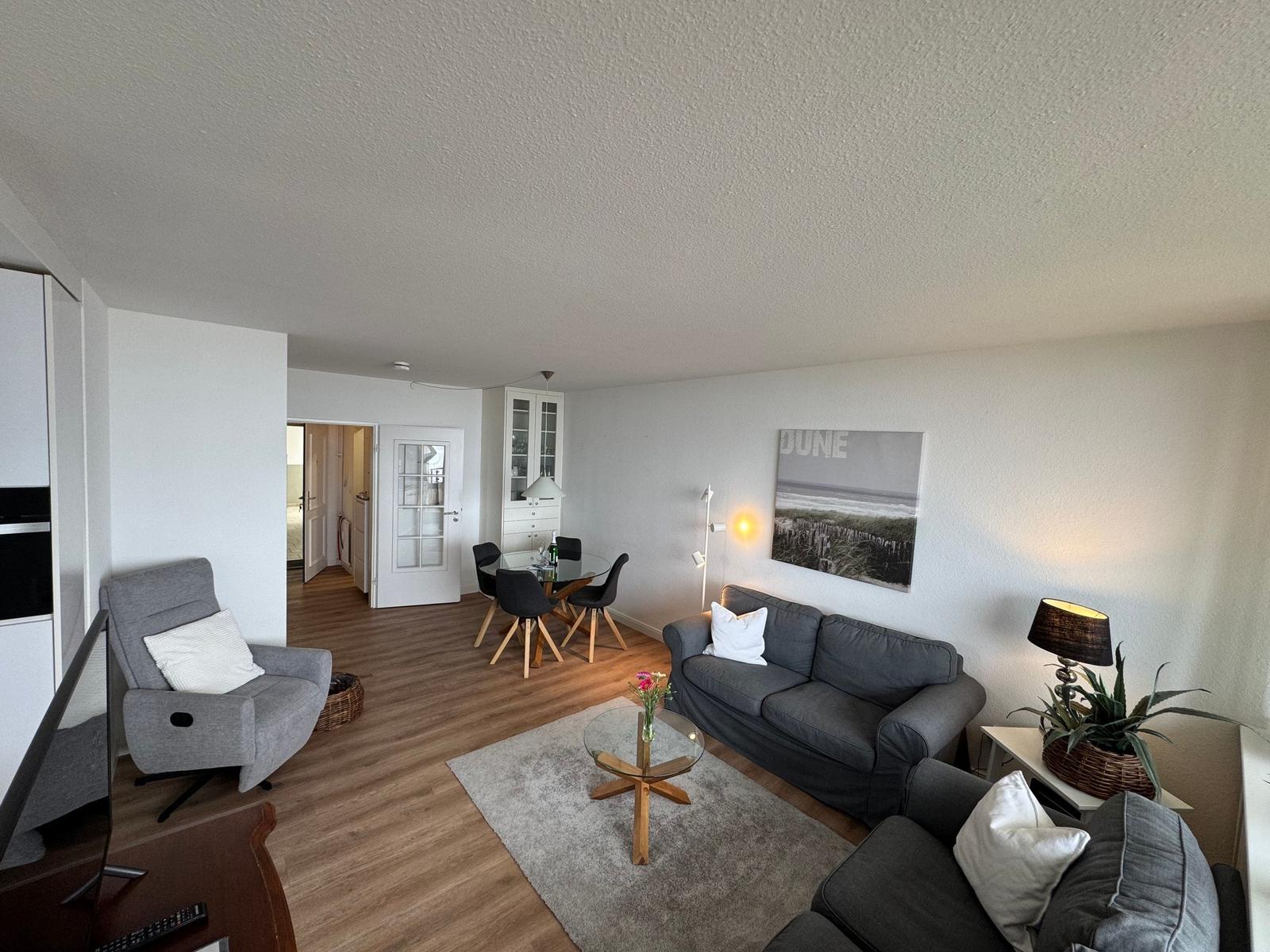 Wohnzimmer mit Sofa, Sessel und Esstisch. Wandbild und Pflanze sichtbar.