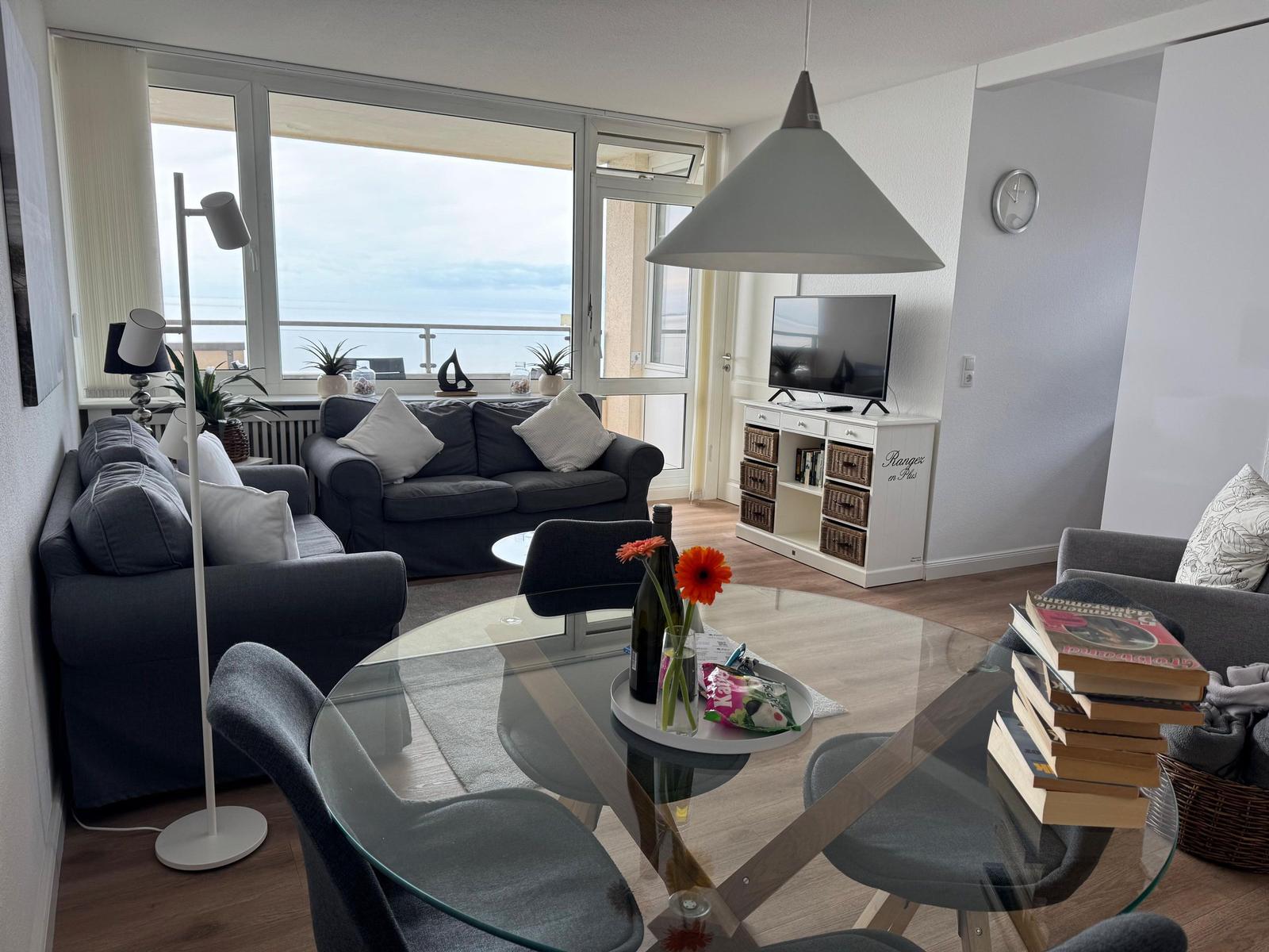 Wohnzimmer mit Sitzgelegenheiten, Glas-Tisch und TV. Balkon mit Meerblick.
