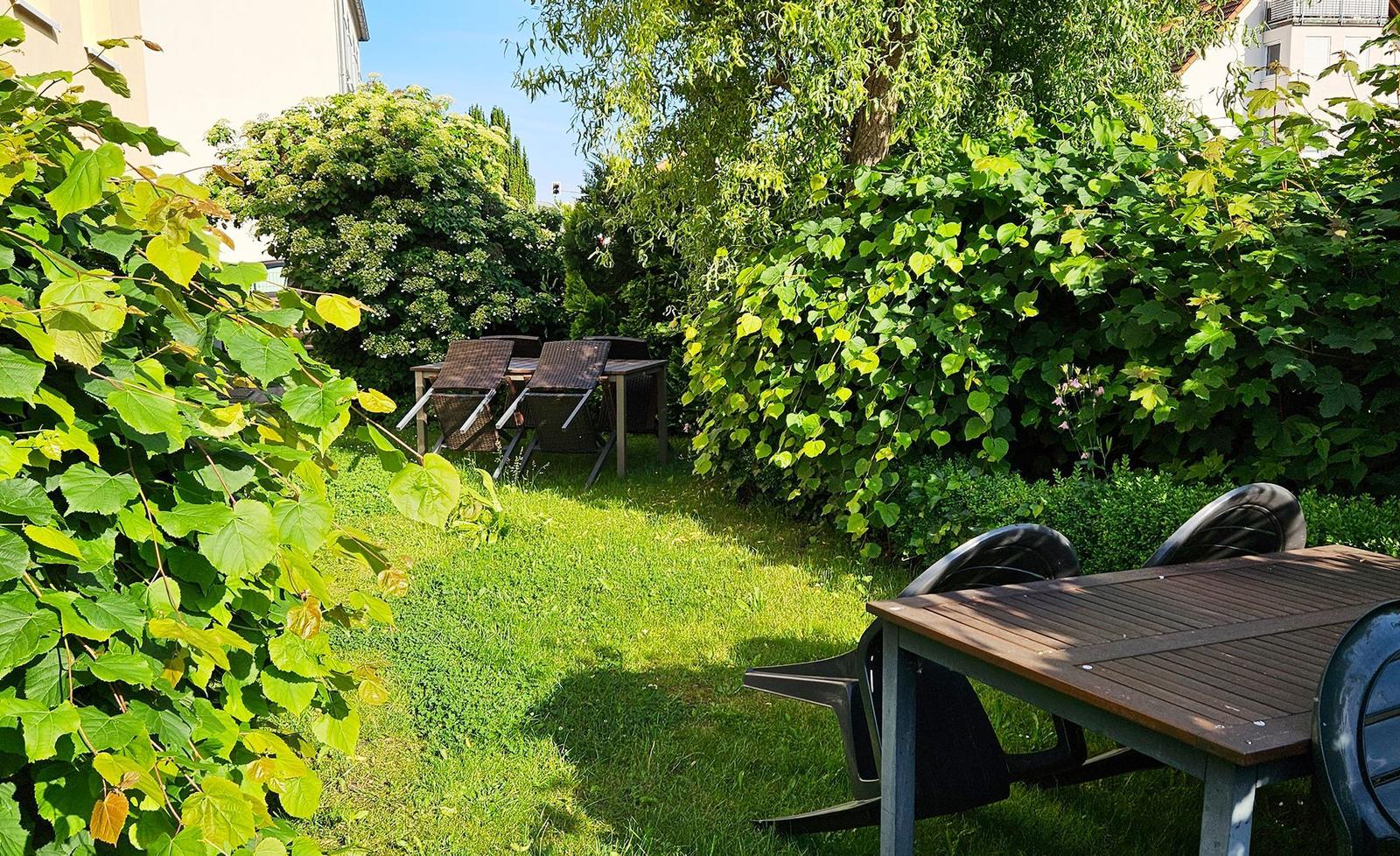 Garten mit grünem Rasen, Bäumen und zwei Holztischen mit Stühlen.