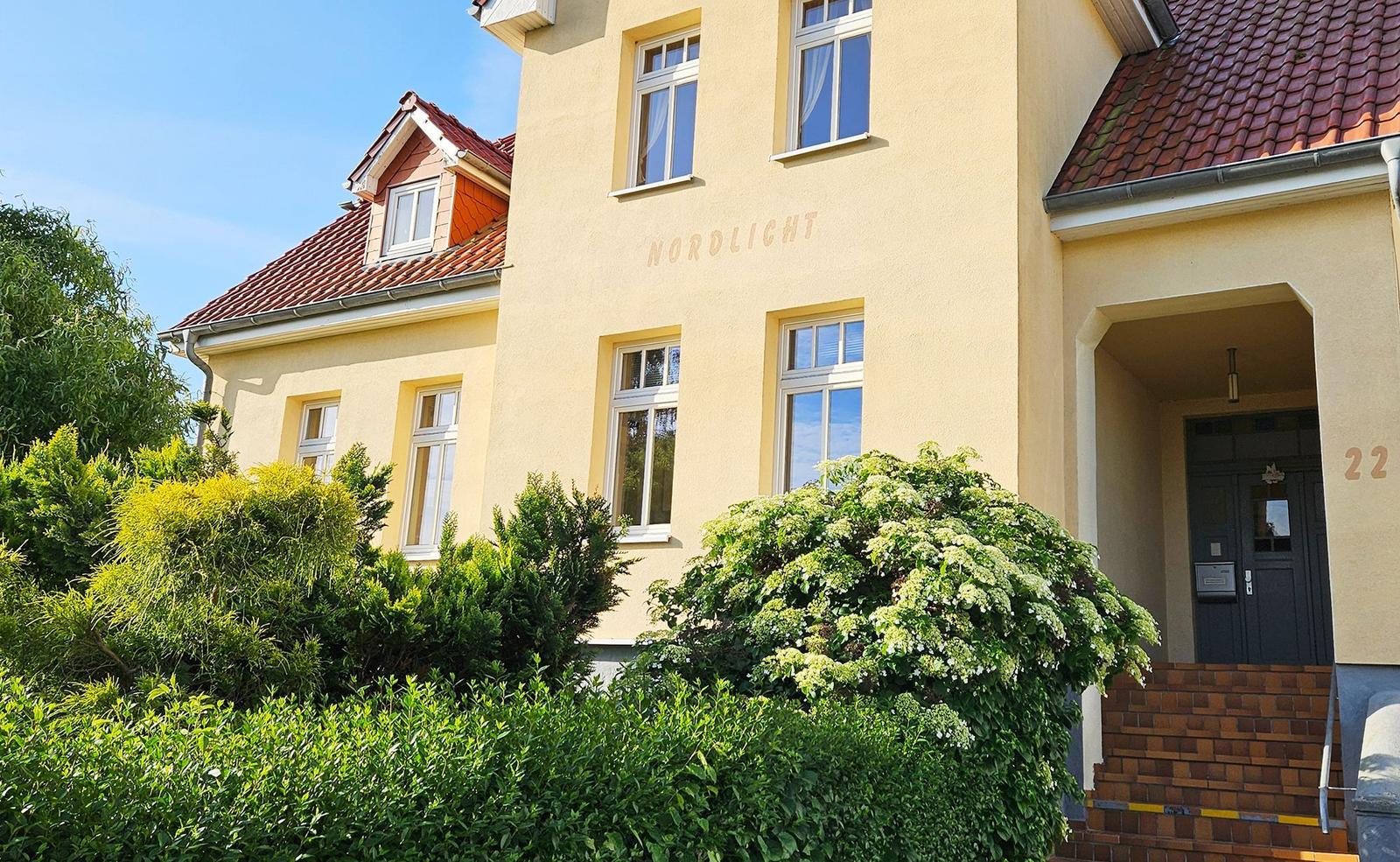 Haus Nordlicht mit Eingang und Garten. Fenster und Dach sichtbar.