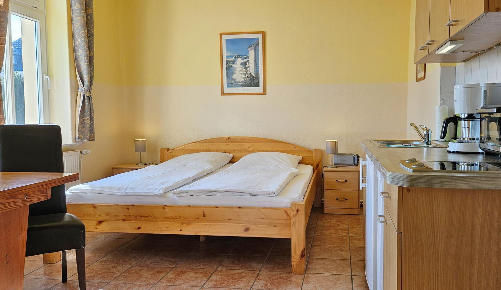 Schlafzimmer mit Bett, Tisch, Küchenzeile und Fenster