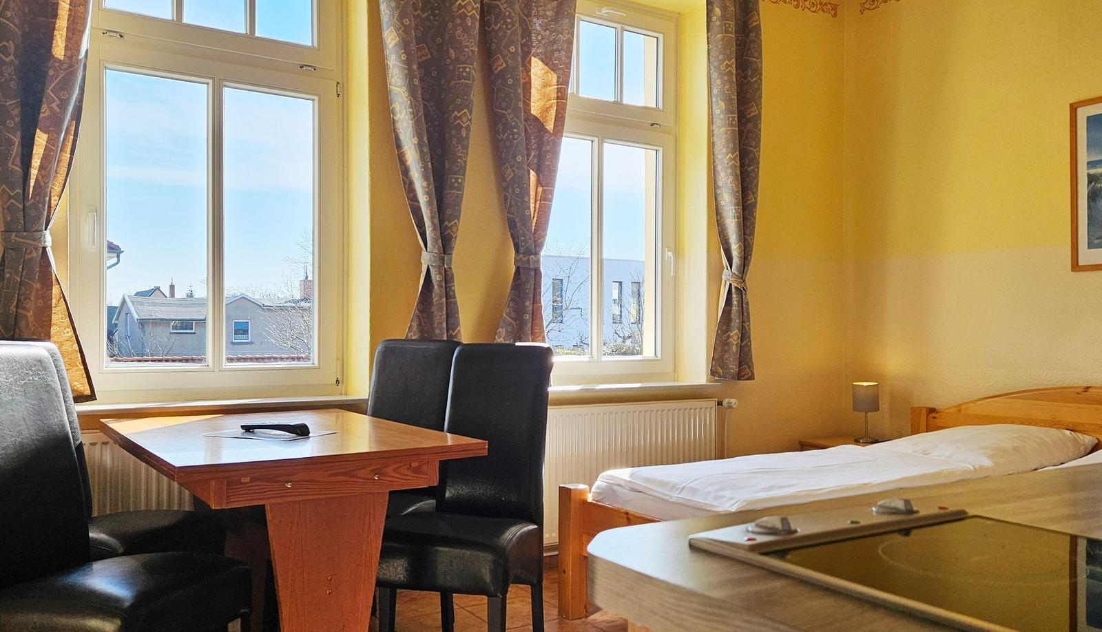 Zimmer mit Bett, Tisch, Stühlen und Fenstern. Blick auf die Straße.