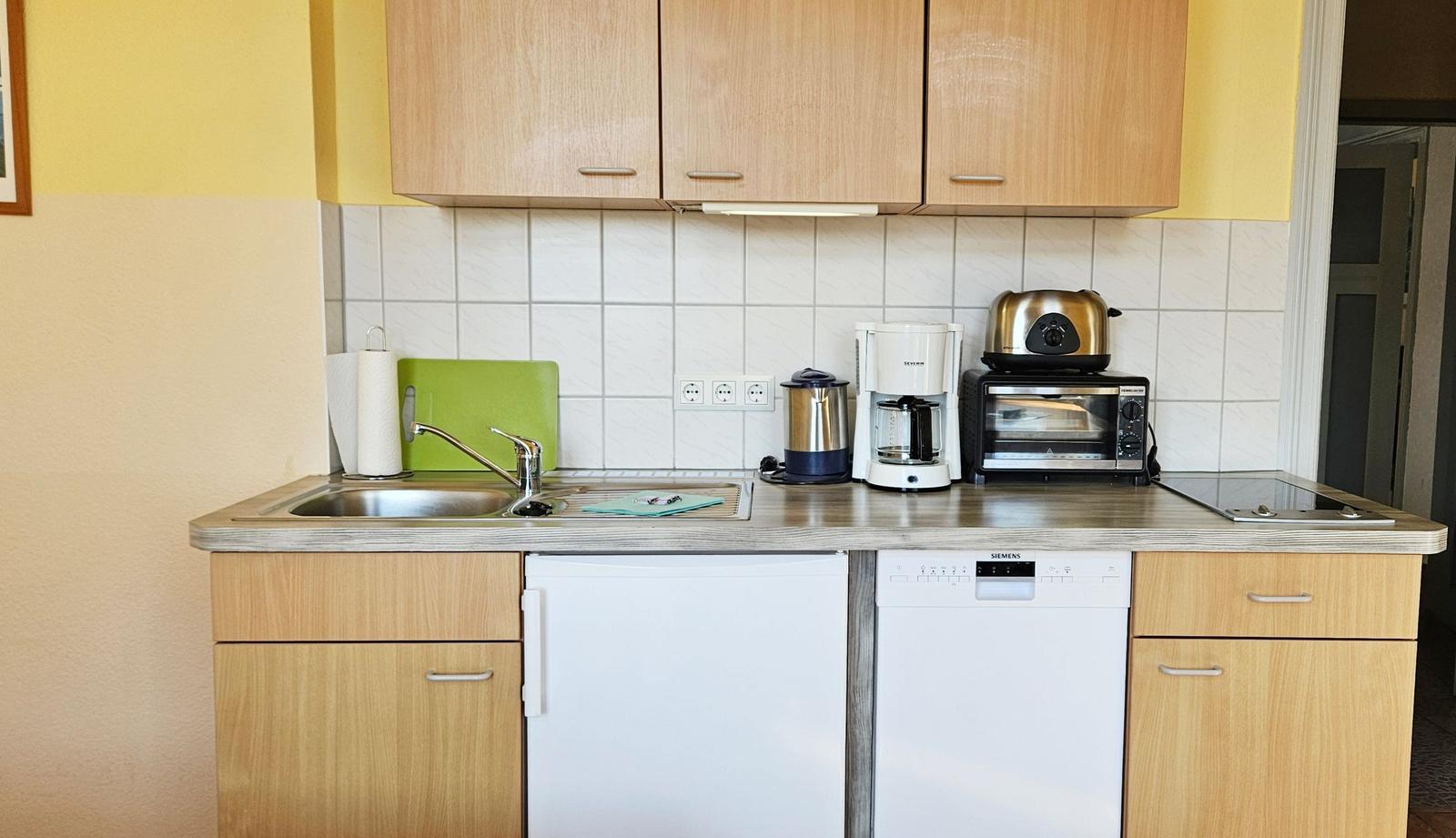Küche mit Spüle, Kühlschrank, Spülmaschine, Kaffeemaschine und Toaster.