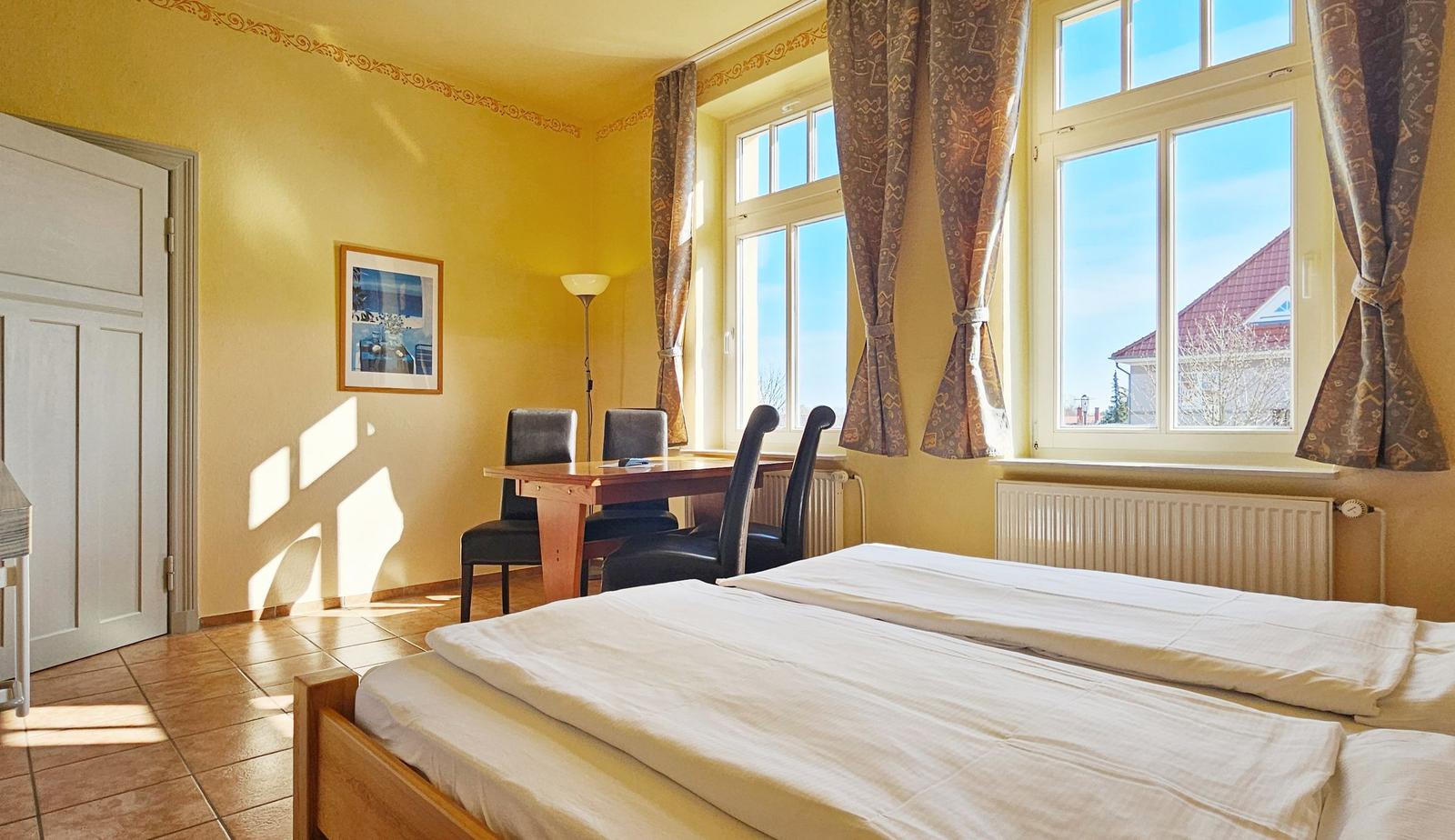 Zimmer mit Doppelbett, Tisch, Stühlen und Fenster mit Blick nach außen.