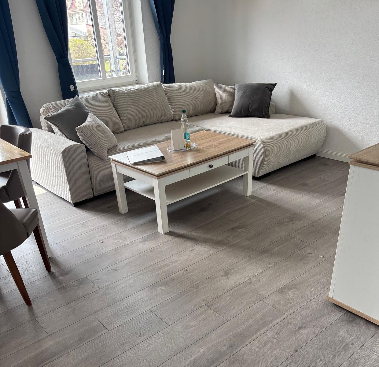 Living room with corner sofa, wooden table, and window with blue curtains.