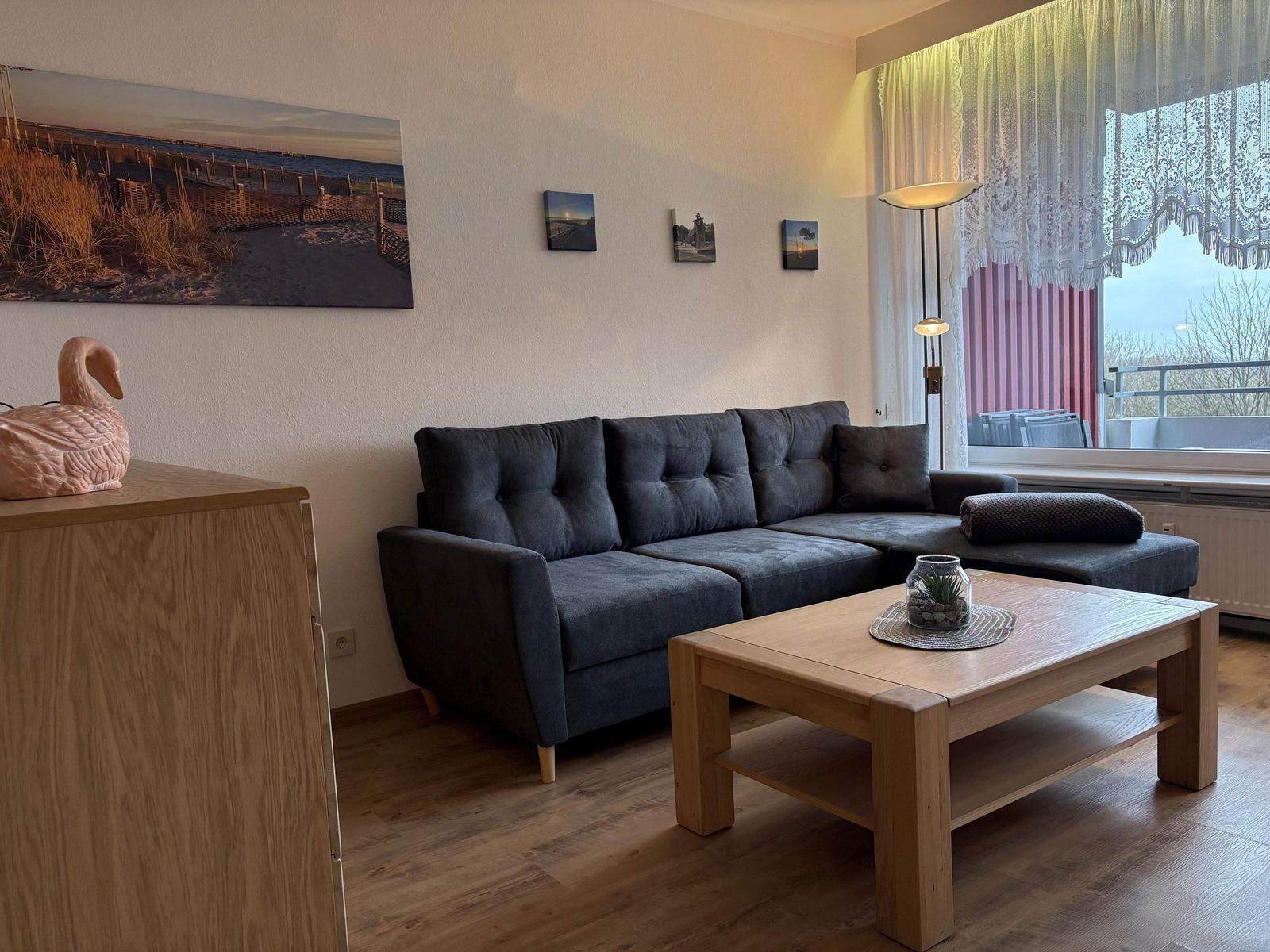 Ein Wohnzimmer mit grauem Sofa, Holztisch und Wandbildern.