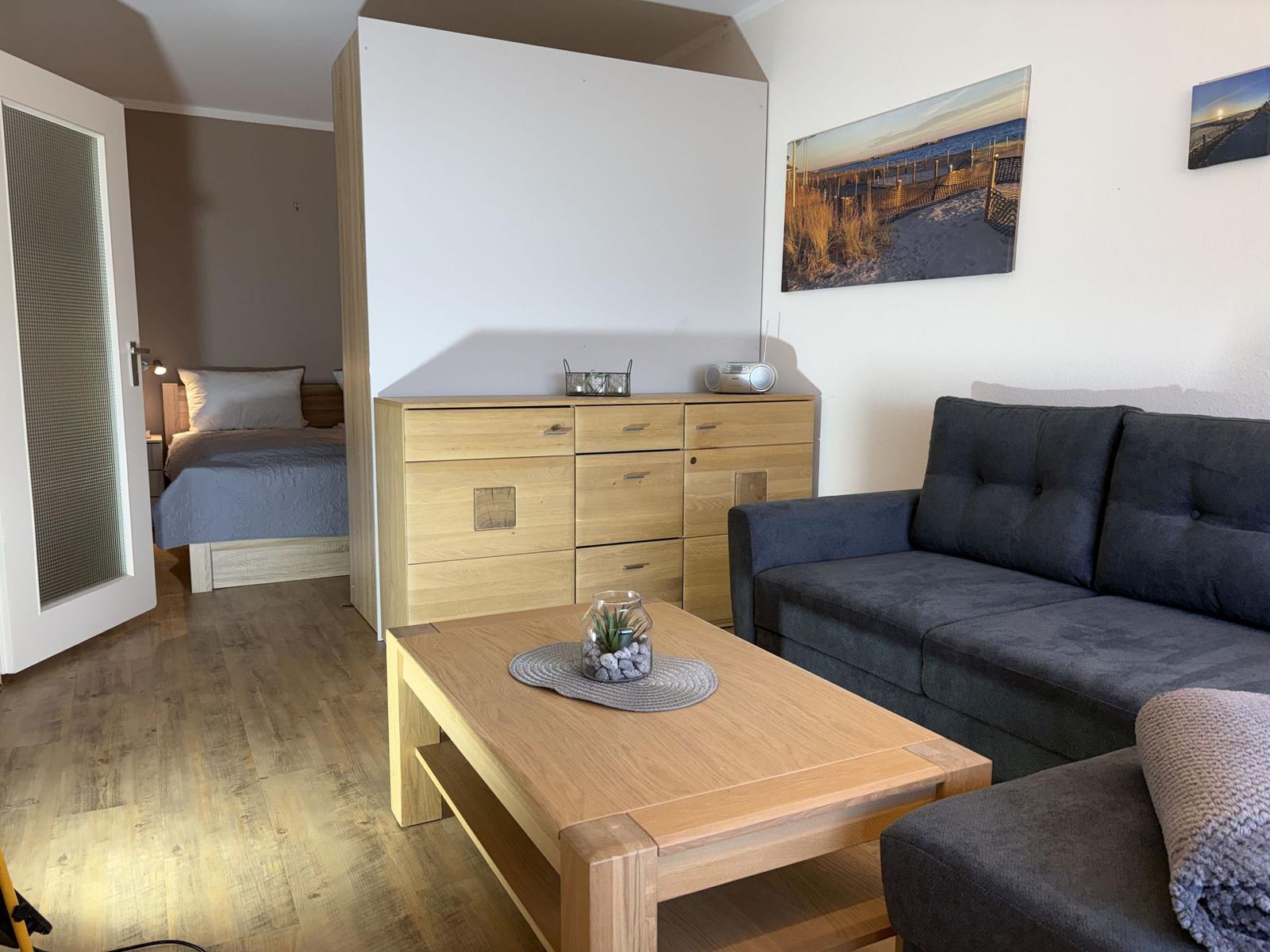 Wohnbereich mit Sofa, Couchtisch und Schlafzimmer im Hintergrund.