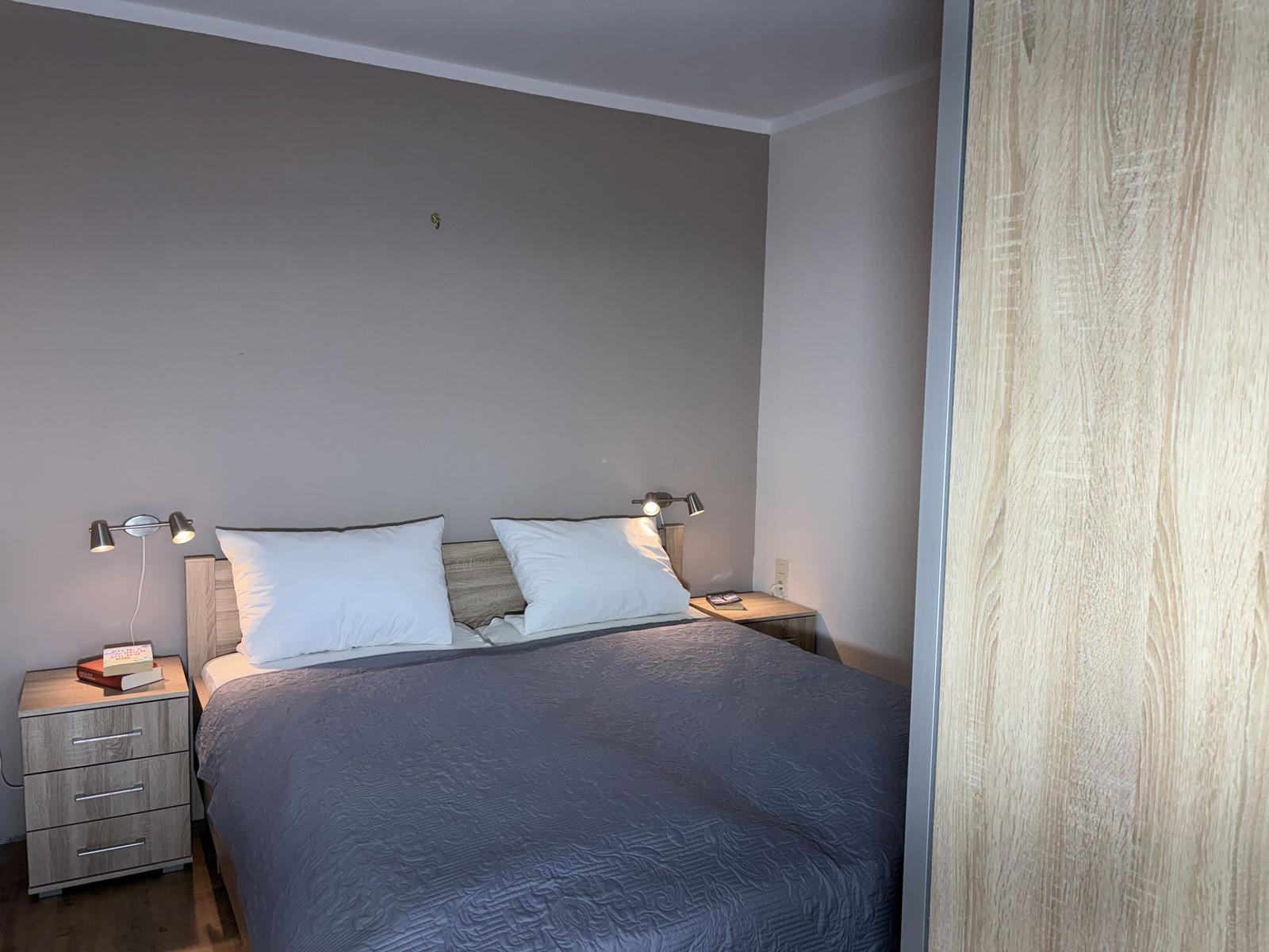 Doppelbett mit zwei Nachttischen und Stehlampe. Holzschrank rechts.