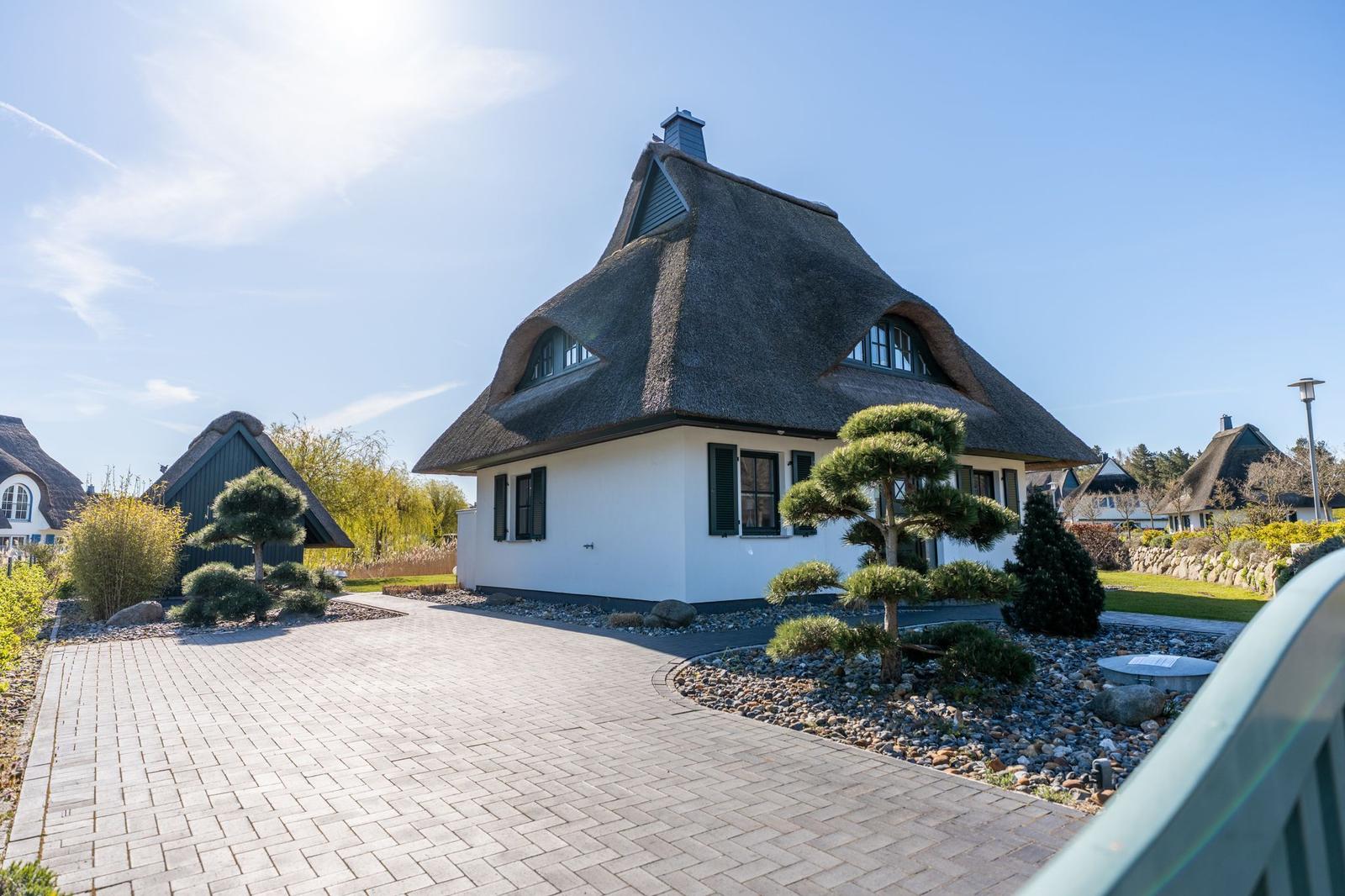 Wohnhaus mit strohgedecktem Dach und gepflastertem Vorplatz.