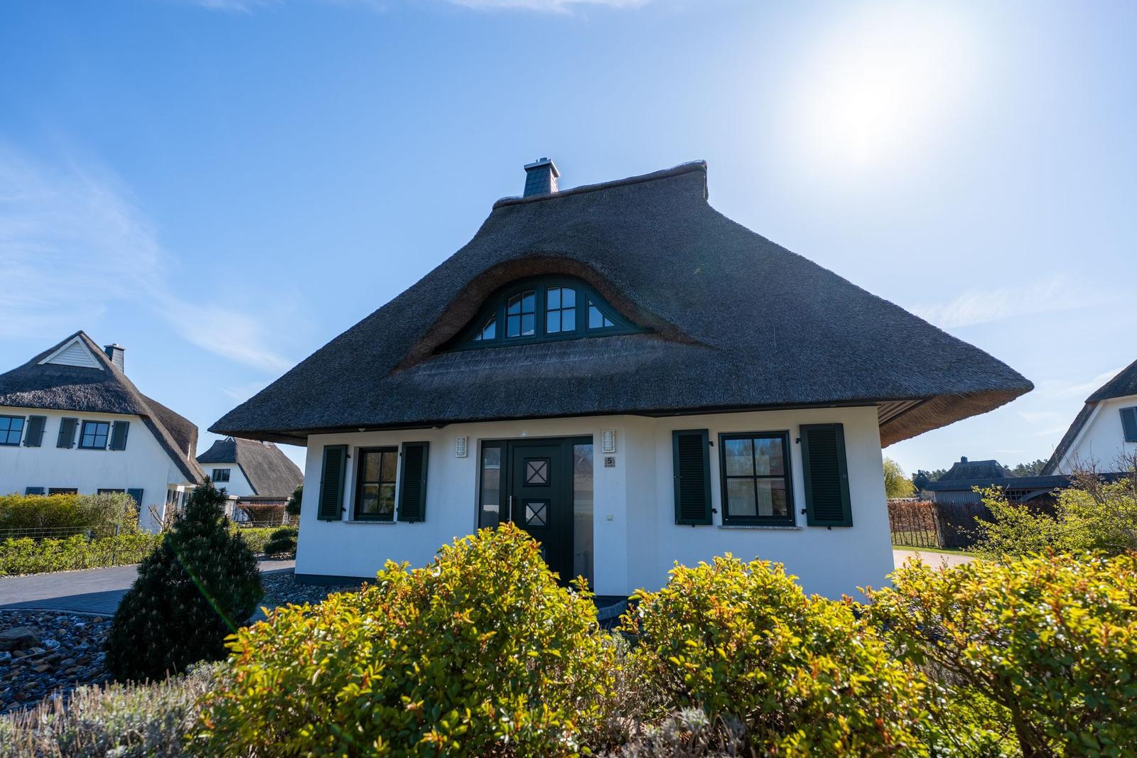 Wohnhaus mit strohgedecktem Dach und grünen Fensterläden.