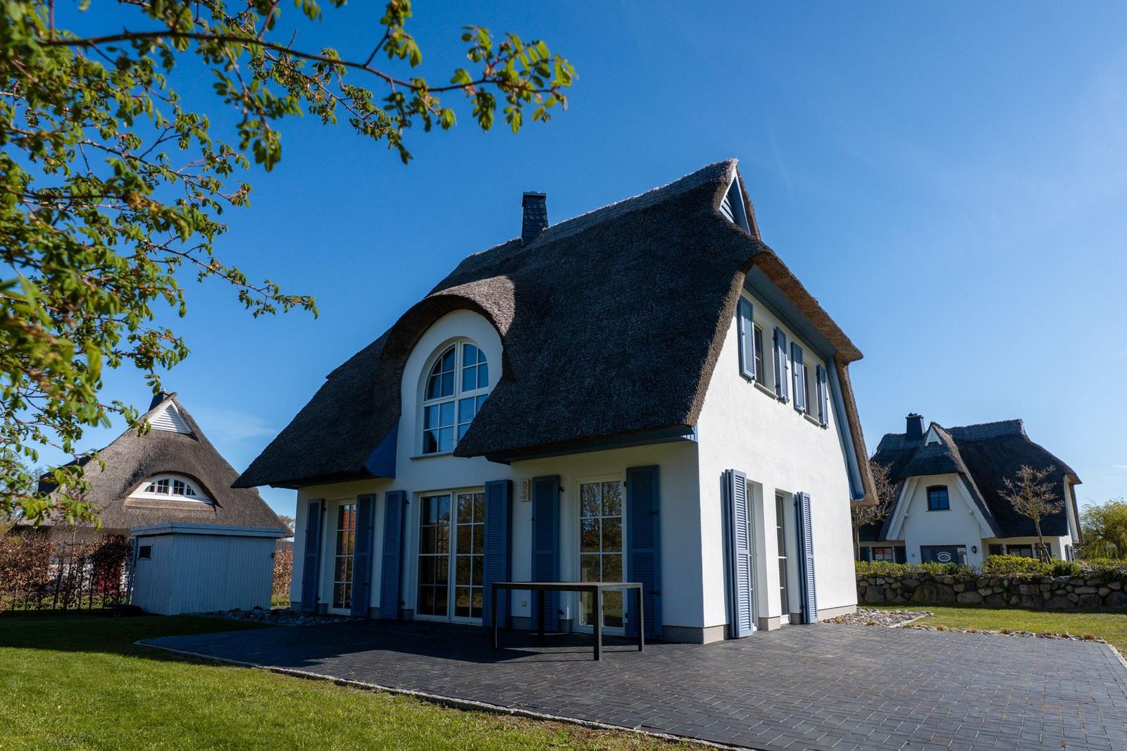 Haus mit strohgedecktem Dach, blauen Fensterläden und großem Fenster.