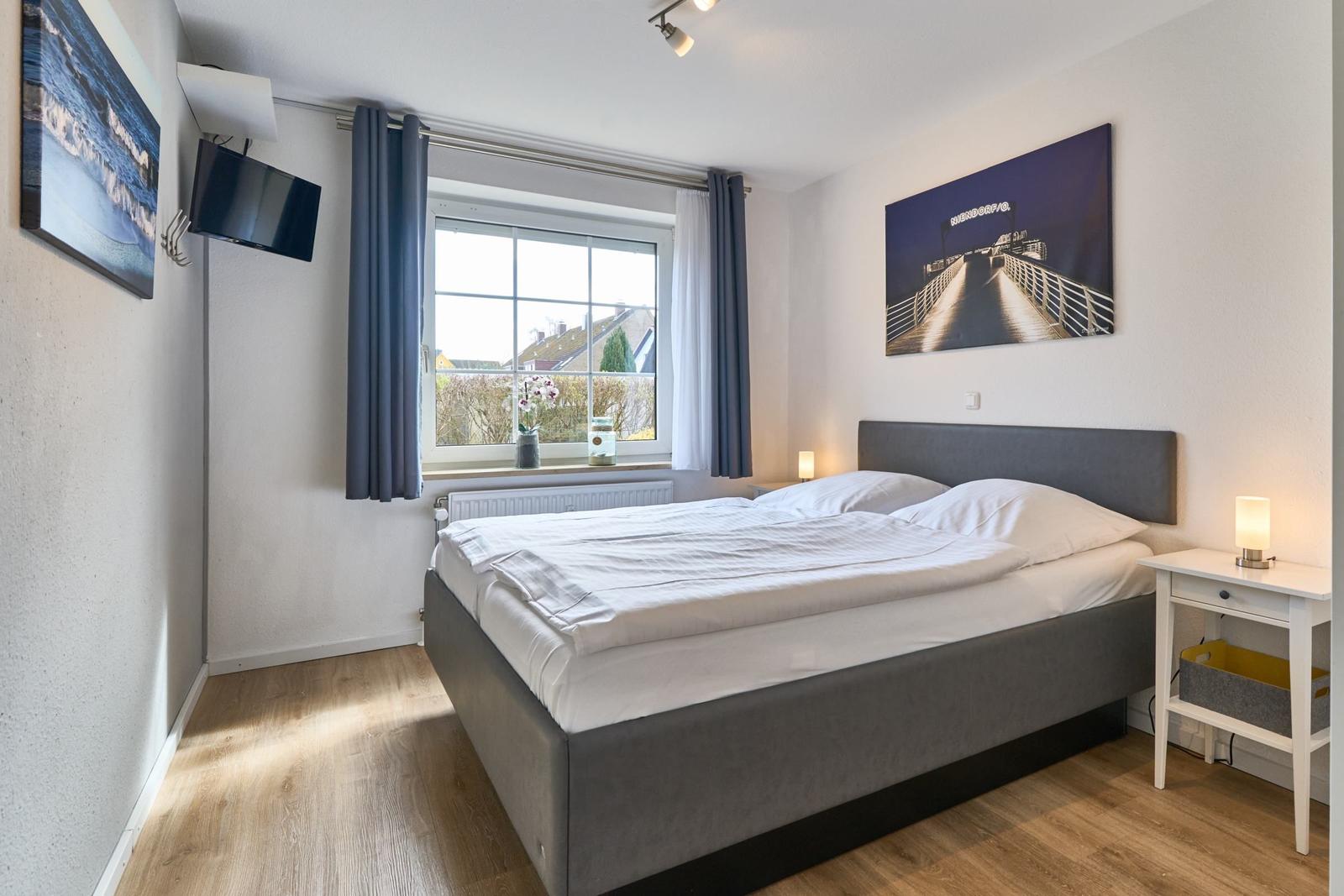Schlafzimmer mit Doppelbett, Fenster, Nachttisch und Wandbild.