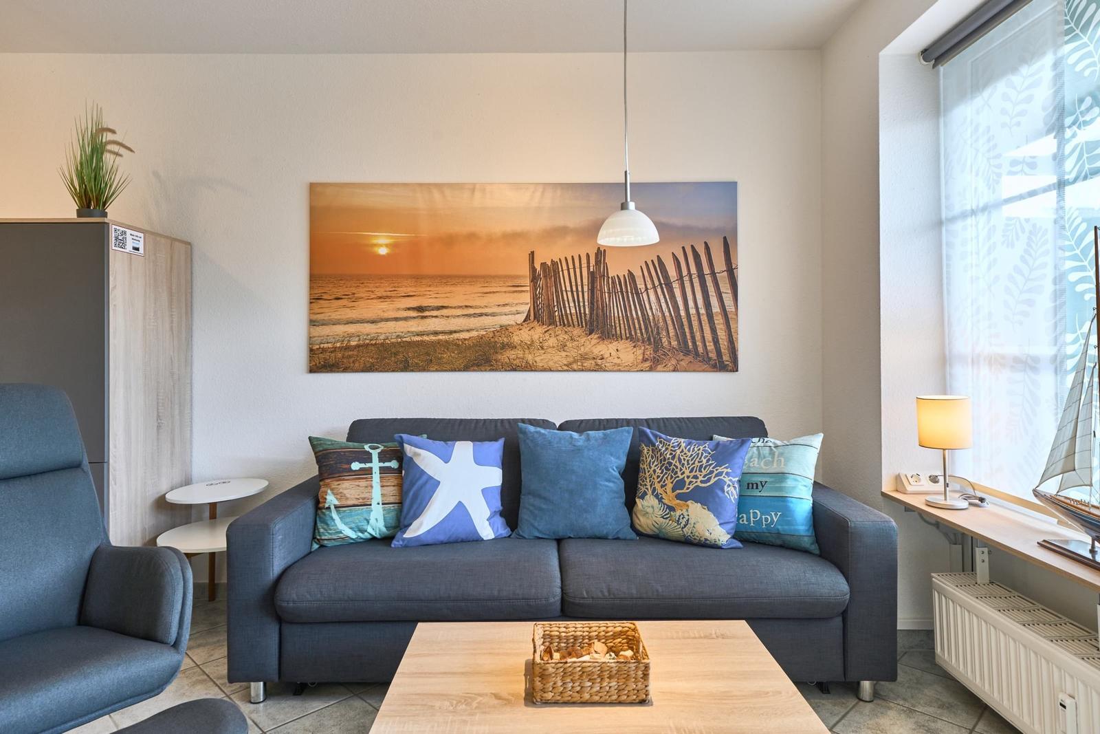 Ein Wohnzimmer mit Sofa, Kissen und Wandbild. Fenster mit Vorhängen und Tischlampe.