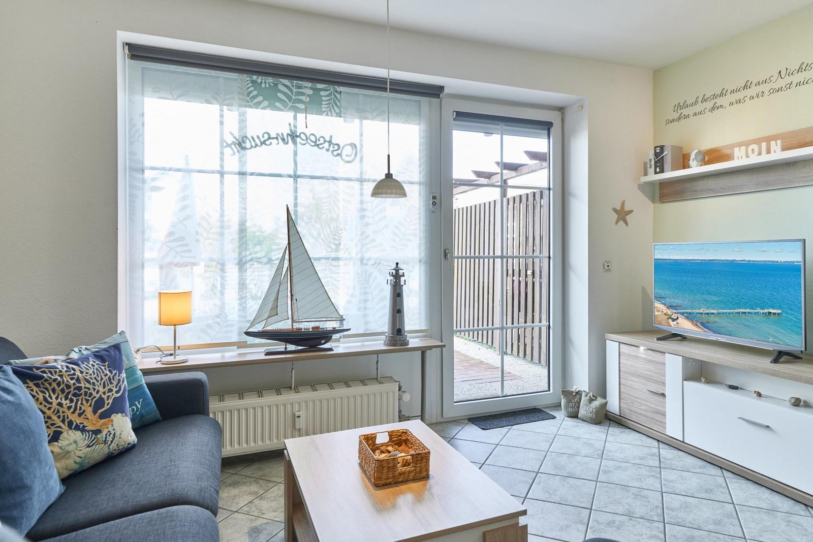 Wohnzimmer mit Sofa, Fernseher und Fenster zur Terrasse.