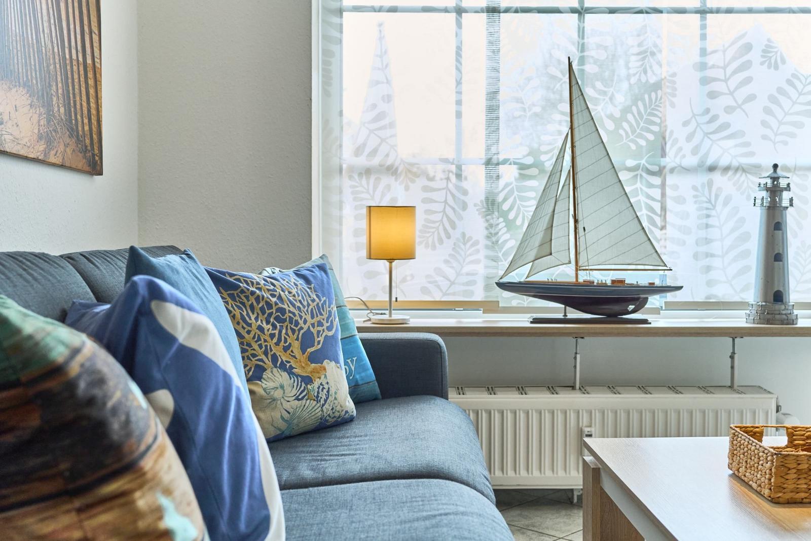 Ein Sofa mit Kissen vor einem Fenster mit Segelboot und Leuchtturmmodell.