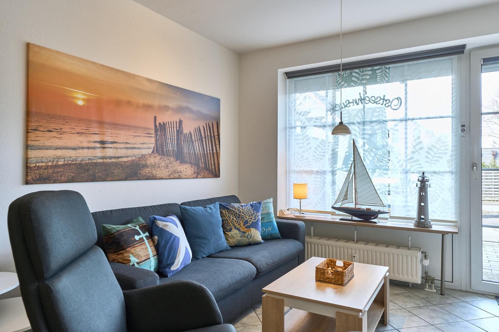 Wohnzimmer mit Sofa, Couchtisch und Fenster mit Blick. Wandbild zeigt Strand.