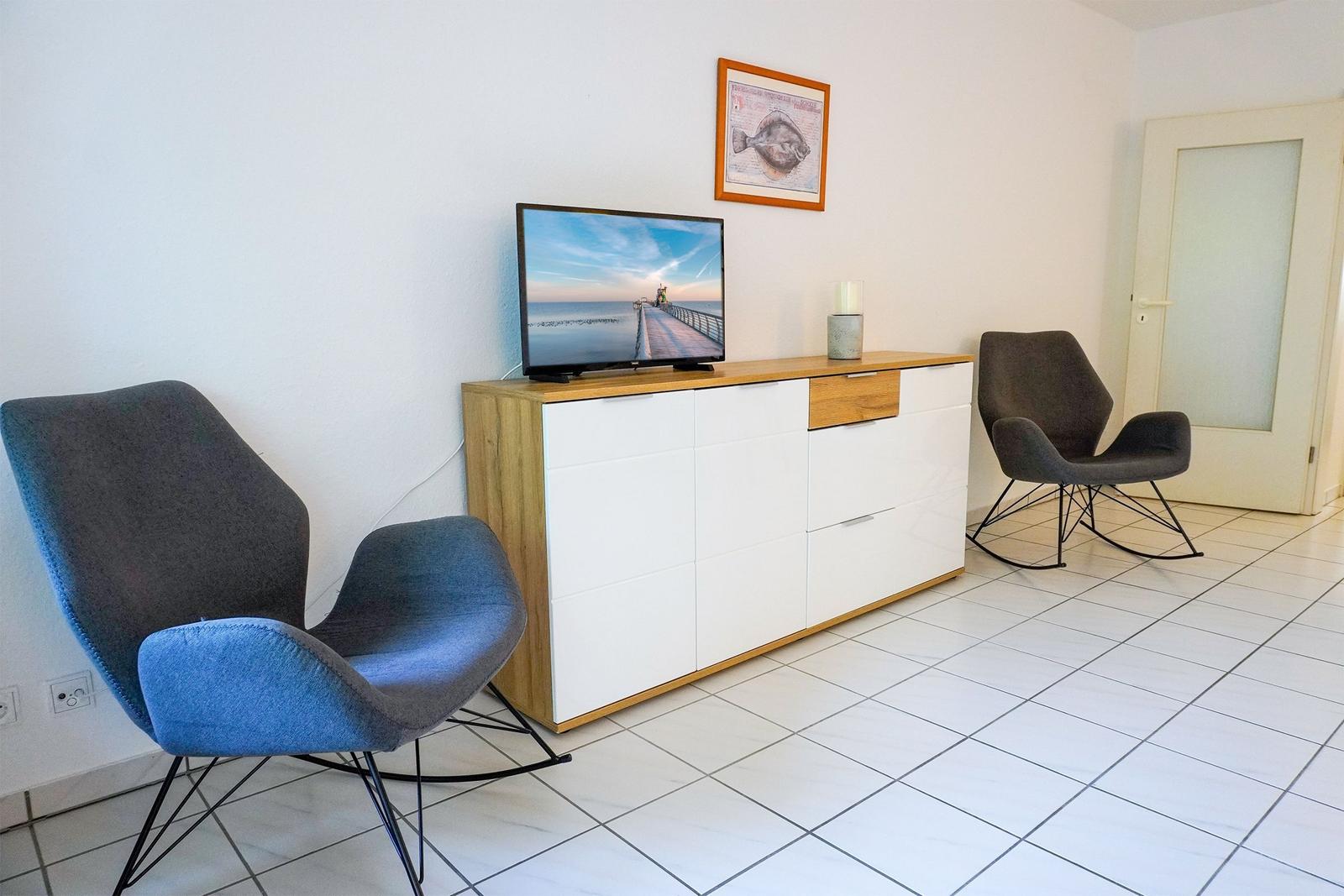 Zwei Sessel und ein TV-Schrank mit Fernseher und Bild an der Wand.