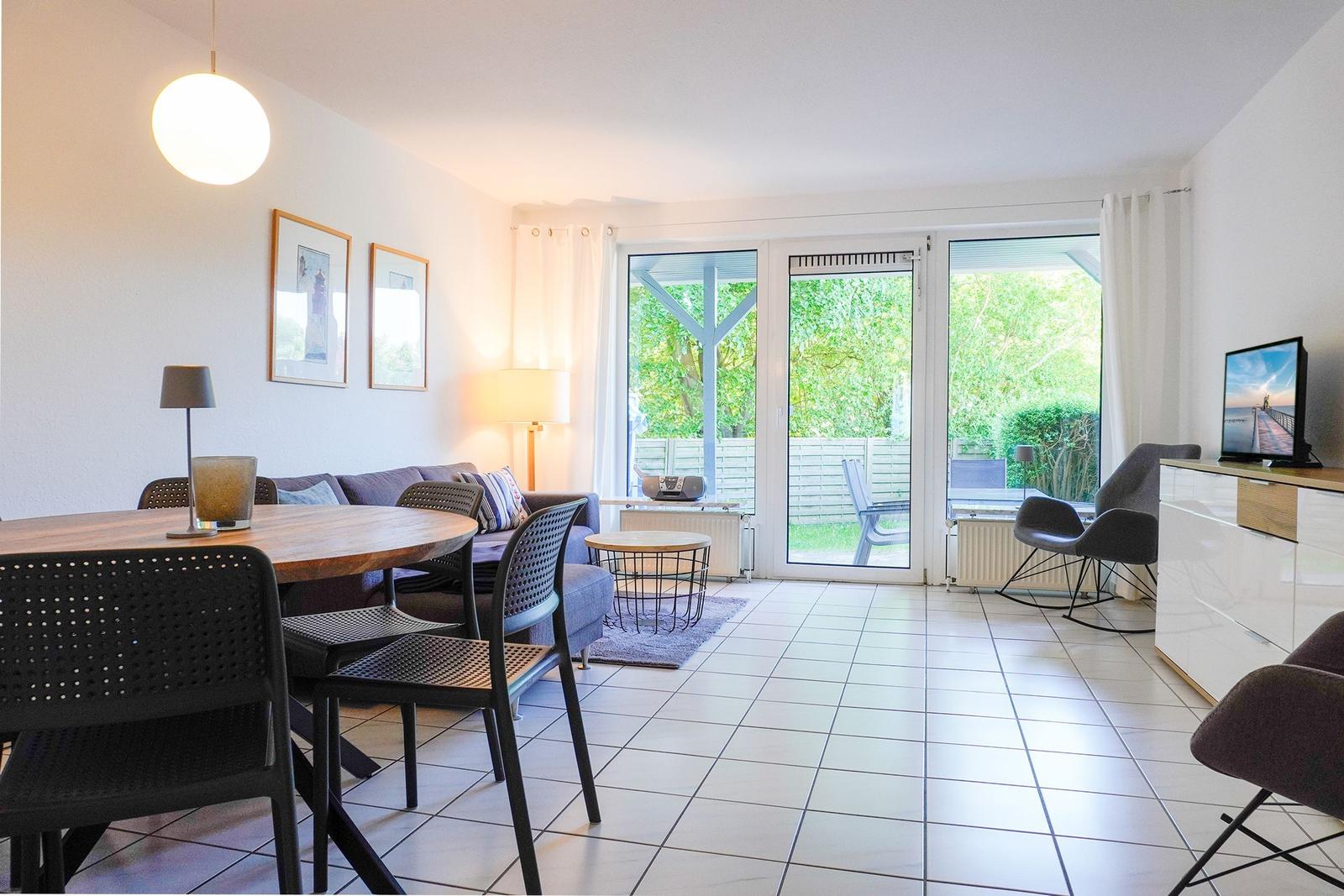 Wohn- und Essbereich mit Blick auf Garten. Tische, Stühle und Sofa sind vorhanden.