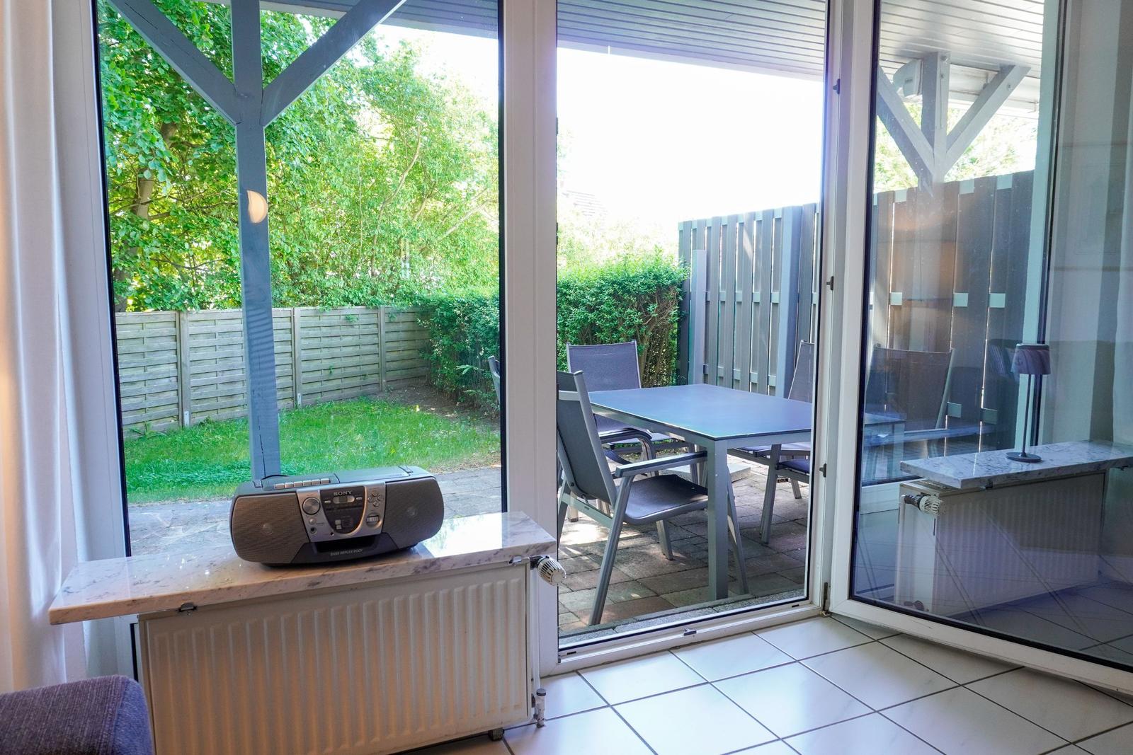 Terrasse mit Tisch und Stühlen, Blick auf Garten mit Zaun und Bäumen.