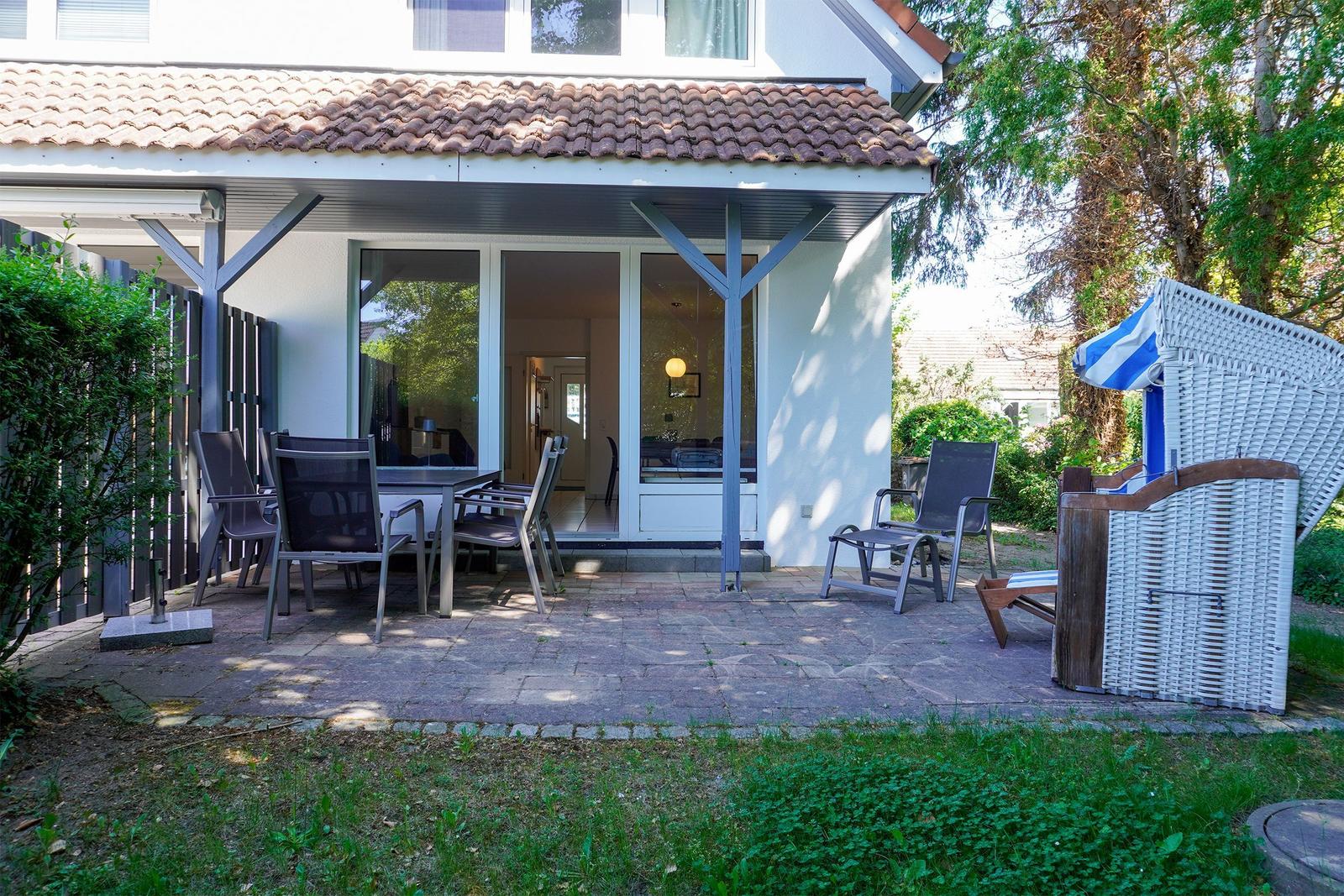 Terrasse mit Sitzgruppe und Strandkorb. Durchgang zur Wohnung. Umgeben von Grün.