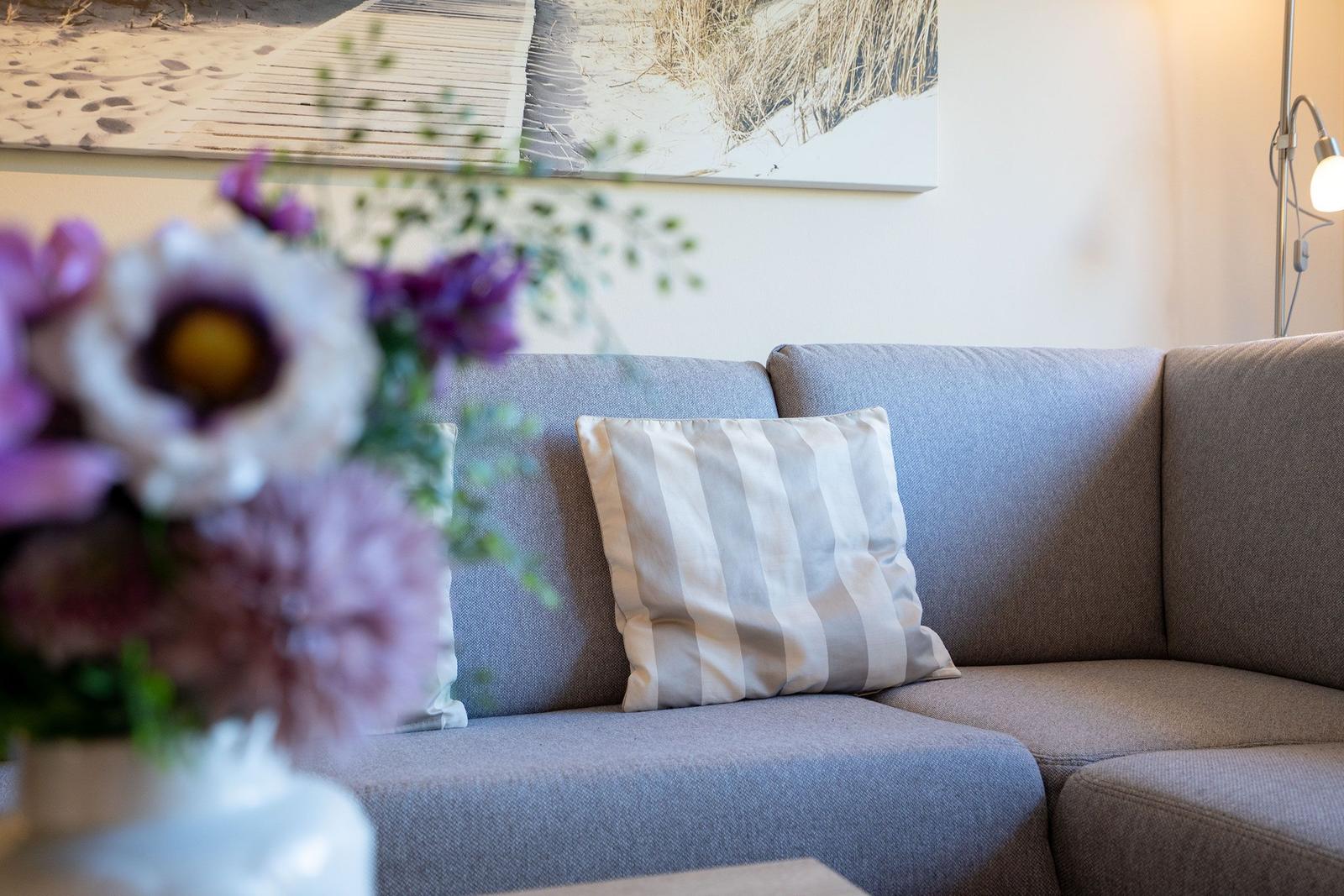 Ein grauer Sofa mit Kissen und Blumen im Vordergrund.