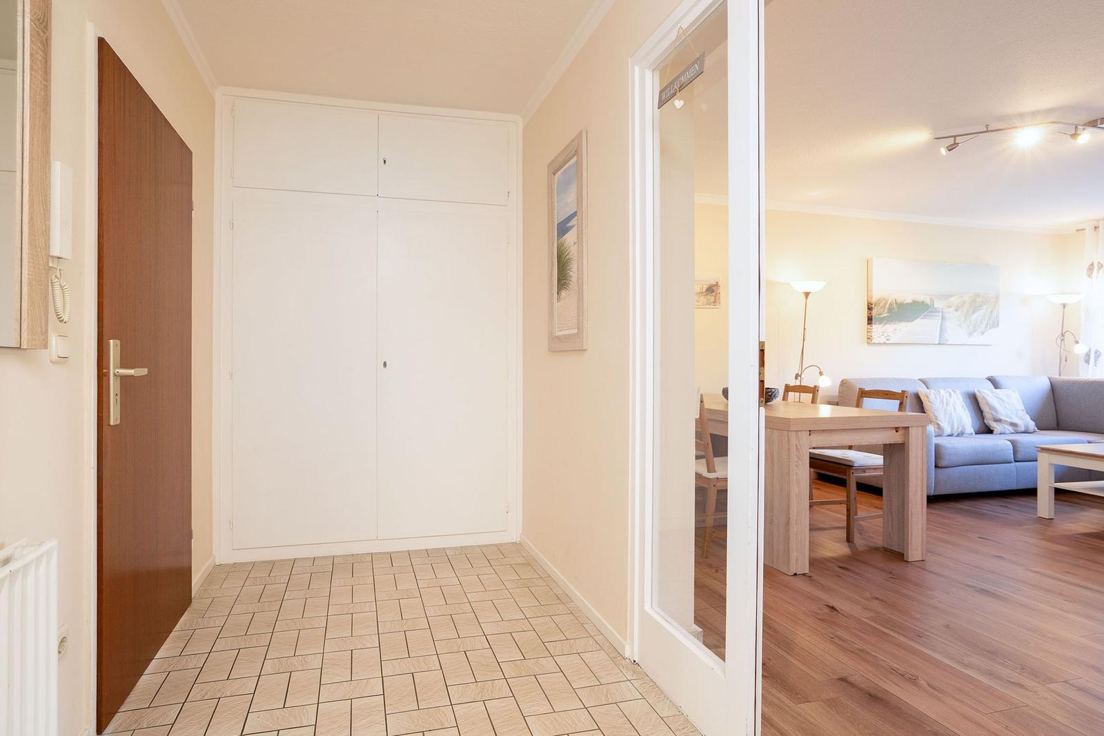 Flur mit Garderobe und Tür zur Wohnküche mit Sofa und Esstisch.