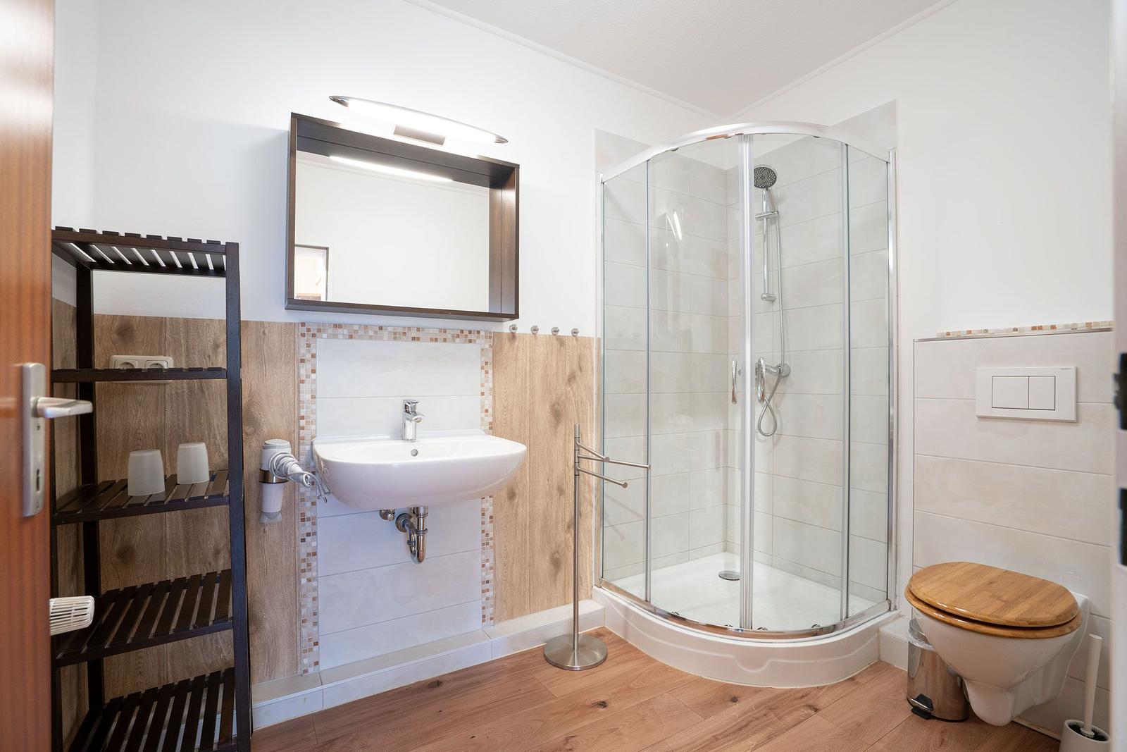 Badezimmer mit Dusche, Waschbecken und Toilette. Holzoptik an Wänden und Boden.