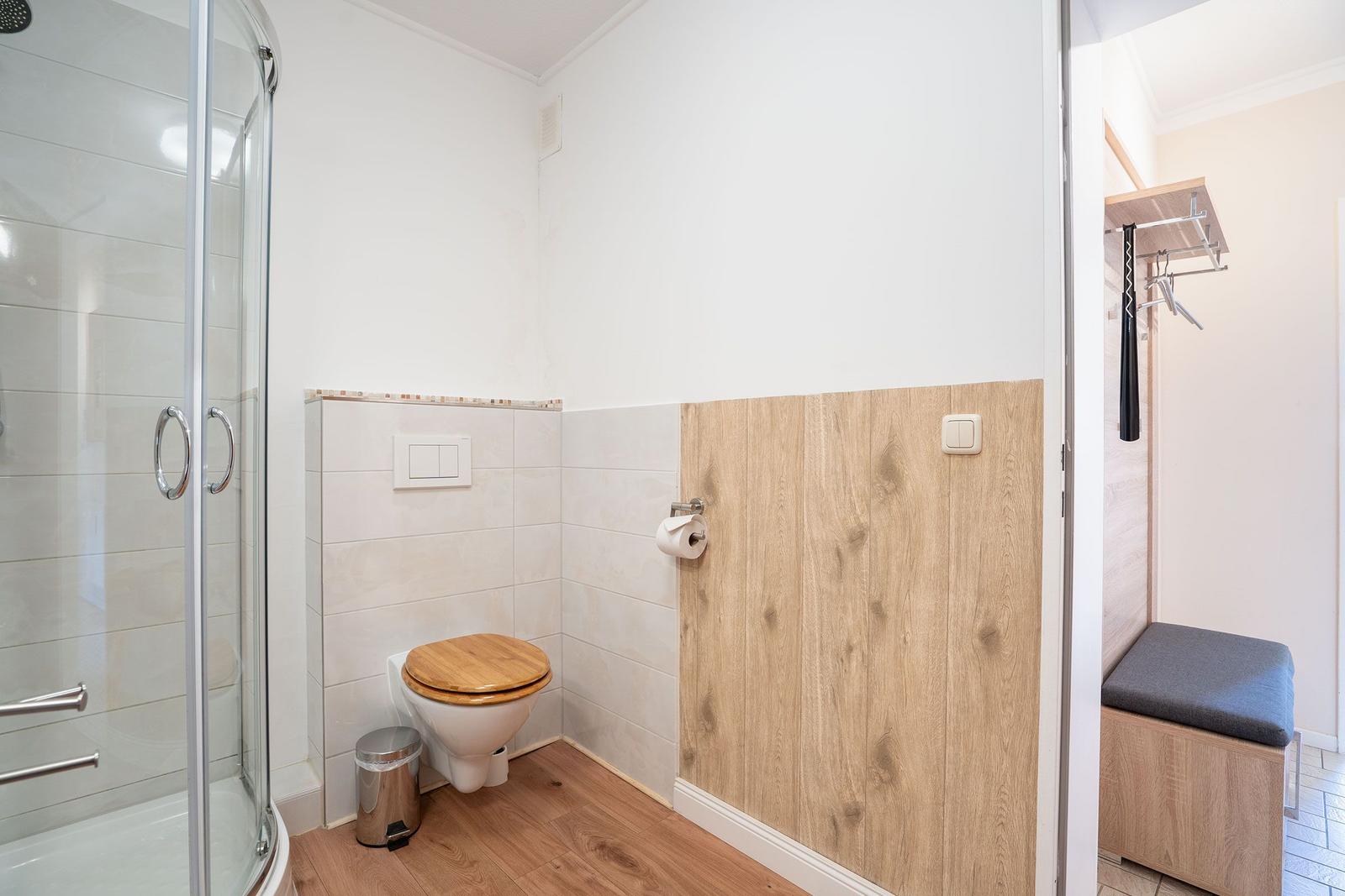 Badezimmer mit Dusche, Toilette und Holzwand
