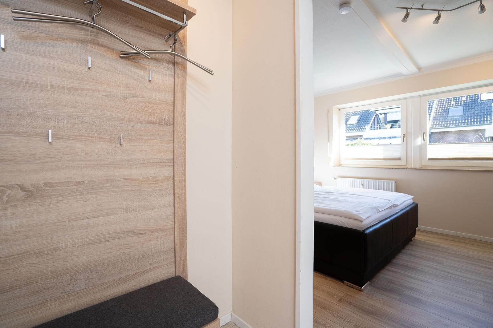 Schlafzimmer mit Bett und Fenster. Ankleidebereich mit Kleiderständer und Sitzbank.