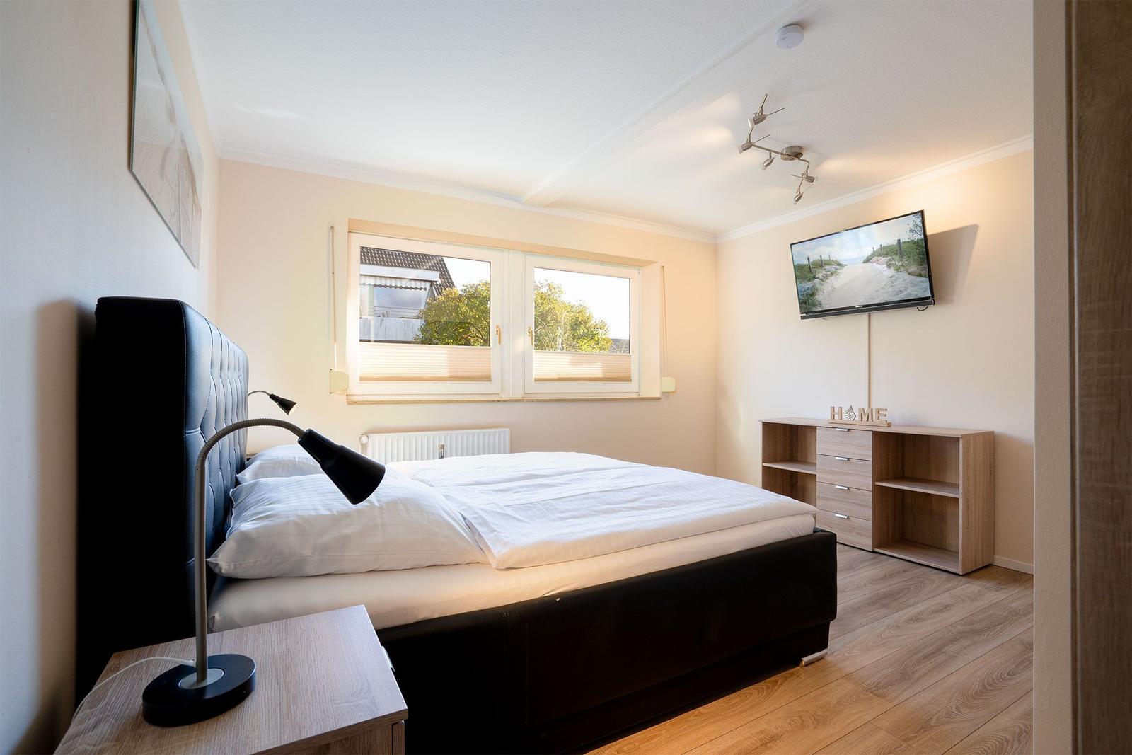 Schlafzimmer mit Doppelbett, Fenster, Fernseher und Nachttisch.