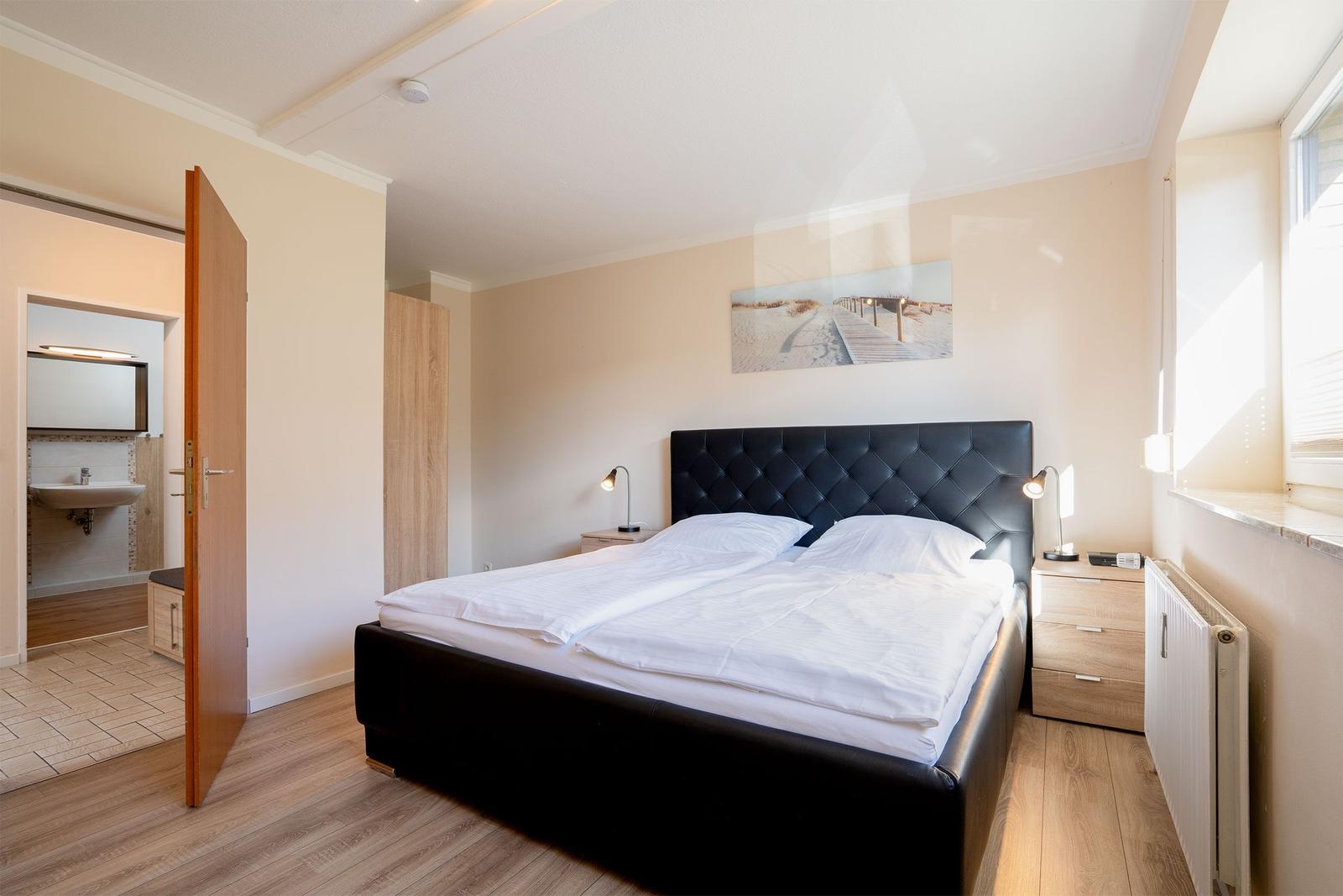 Schlafzimmer mit Doppelbett, Nachttischen und Blick in das Badezimmer.
