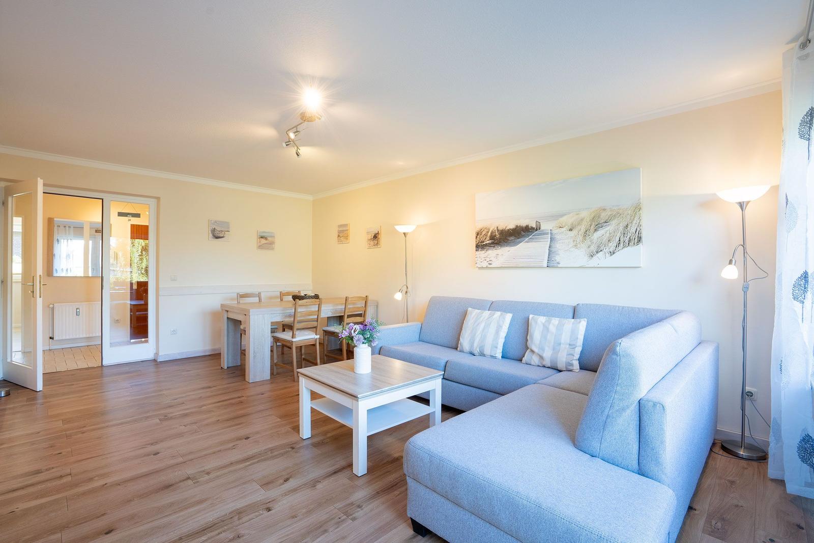 Wohn- und Essbereich mit Sofa, Tisch und Stühlen. Holzboden und Wandbilder.